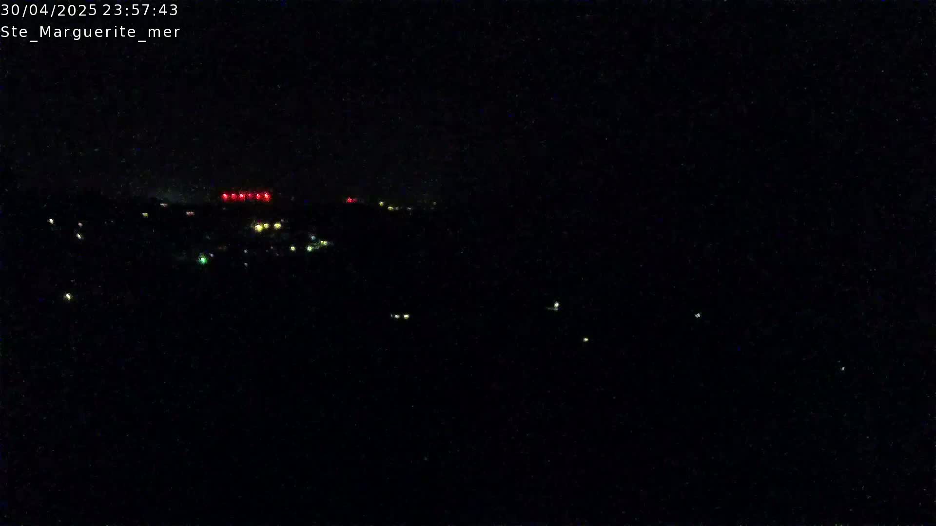 A nighttime long shot shows a dark landscape with scattered small lights and a line of red lights in the distance.