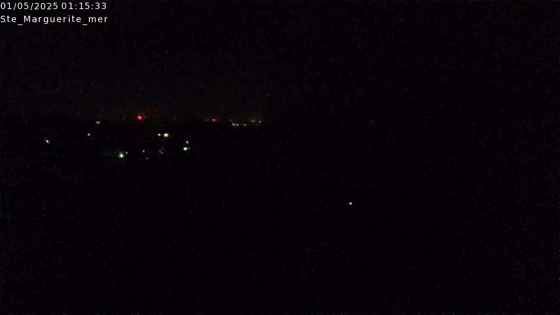 A dark, nighttime scene shows a distant line of faintly glowing lights, likely from a town or city, under a clear, starless sky.