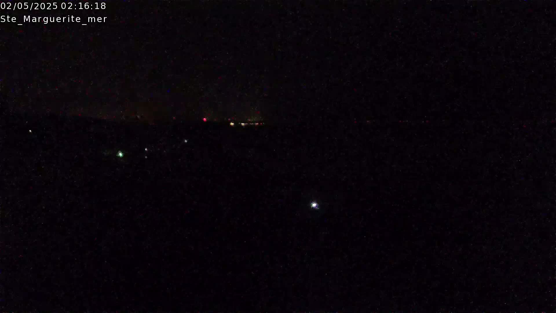 A nighttime view shows a dark landscape with a few faint lights in the distance under a clear, dark sky.
