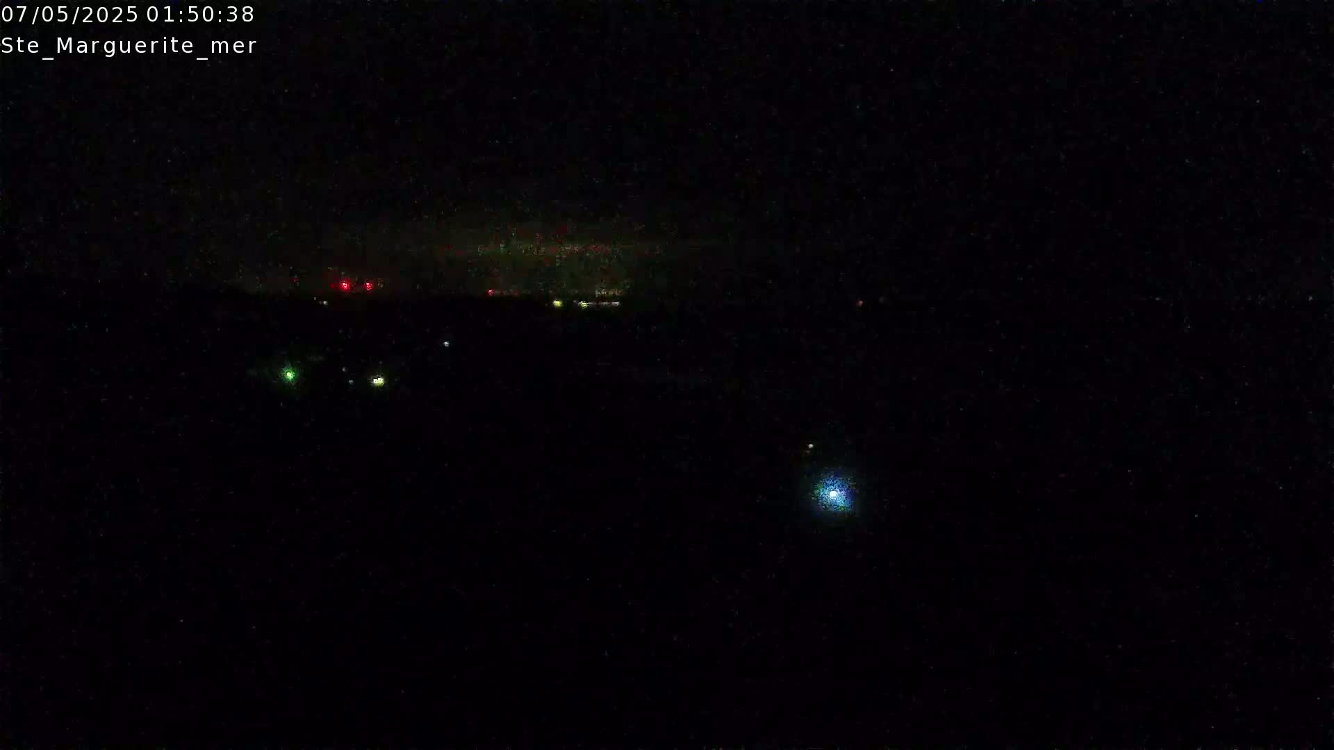 A dark, nighttime scene shows a distant line of faint lights and a few scattered brighter lights, possibly from a town or city, under a mostly clear night sky.