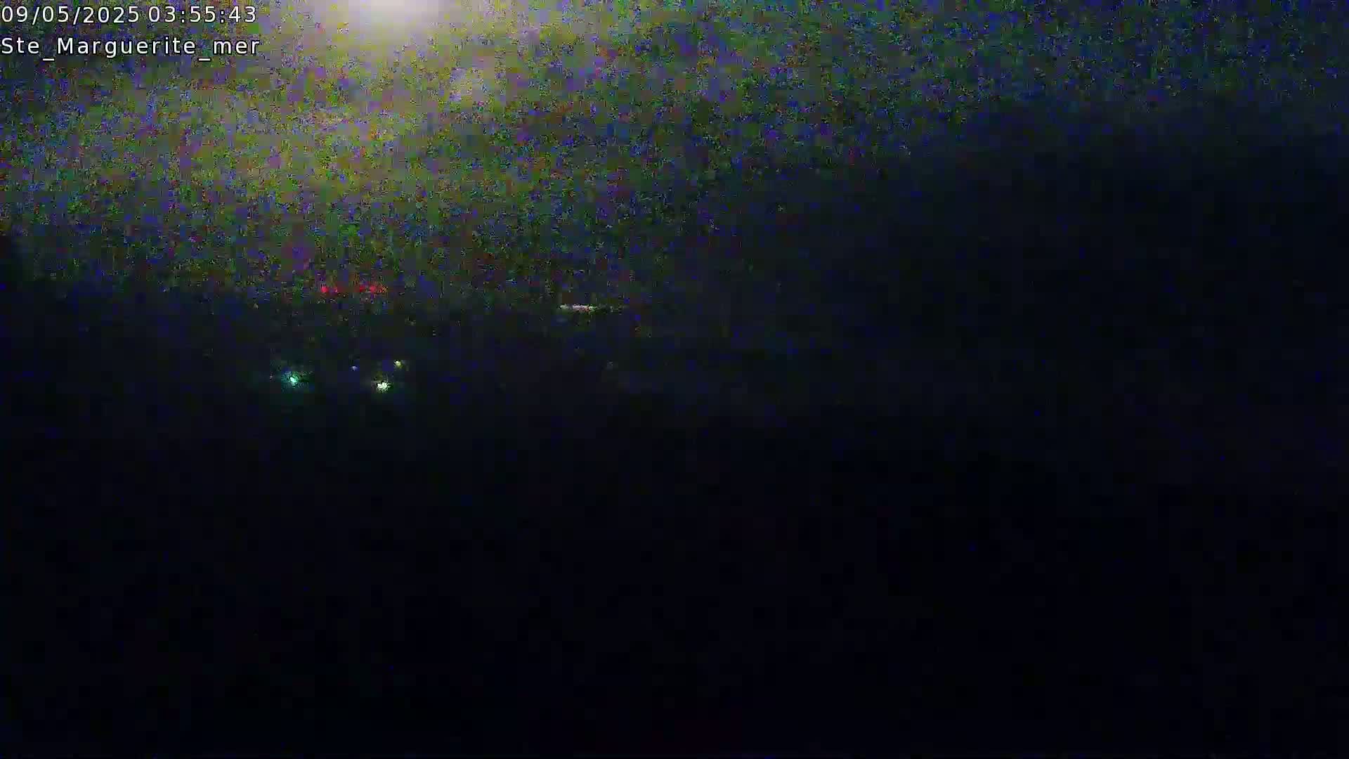 A dark, nighttime scene shows a few distant lights possibly from vehicles or buildings under a cloudy sky.