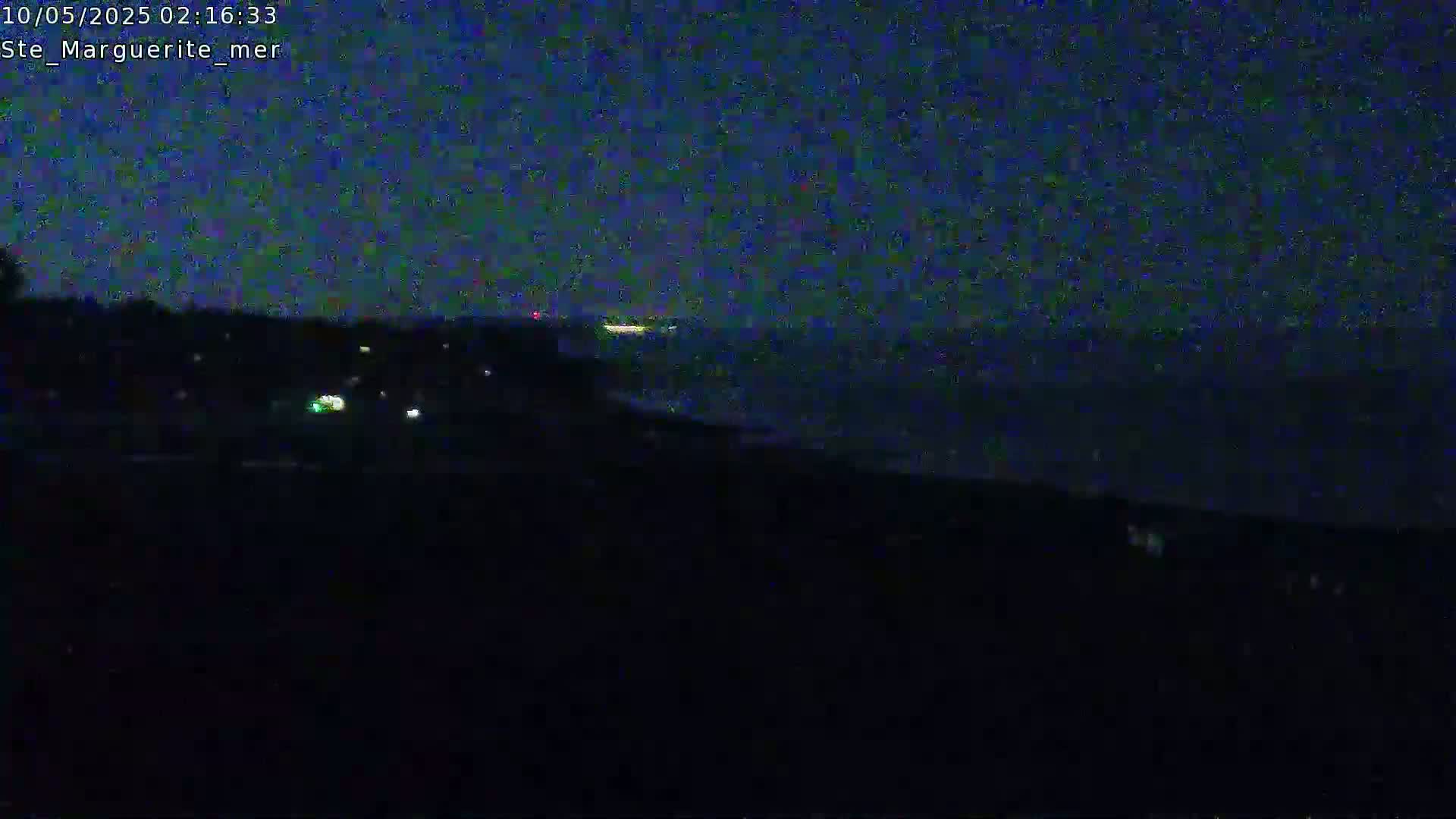 A dark, nighttime view shows a body of water extending to a dark horizon under a mostly clear, dark blue sky.