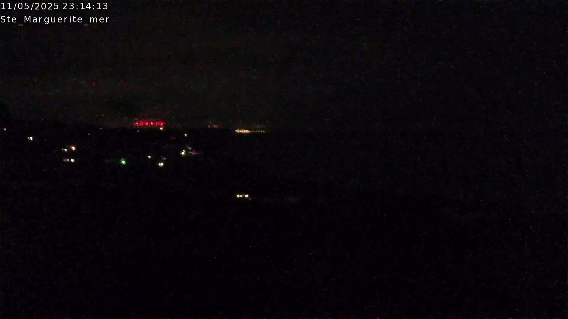 A nighttime, dark view shows a few scattered lights in the distance, likely from a town or city, under a clear, dark sky.