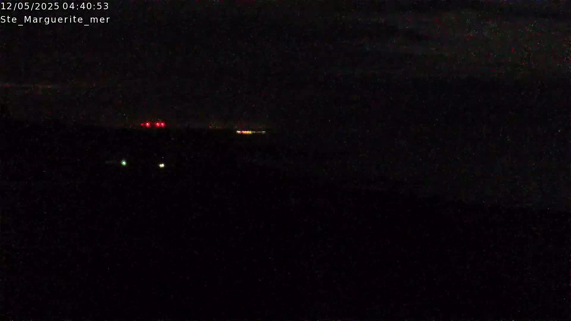 A nighttime, dark scene shows a few small, distant lights on the horizon under a cloudy sky.