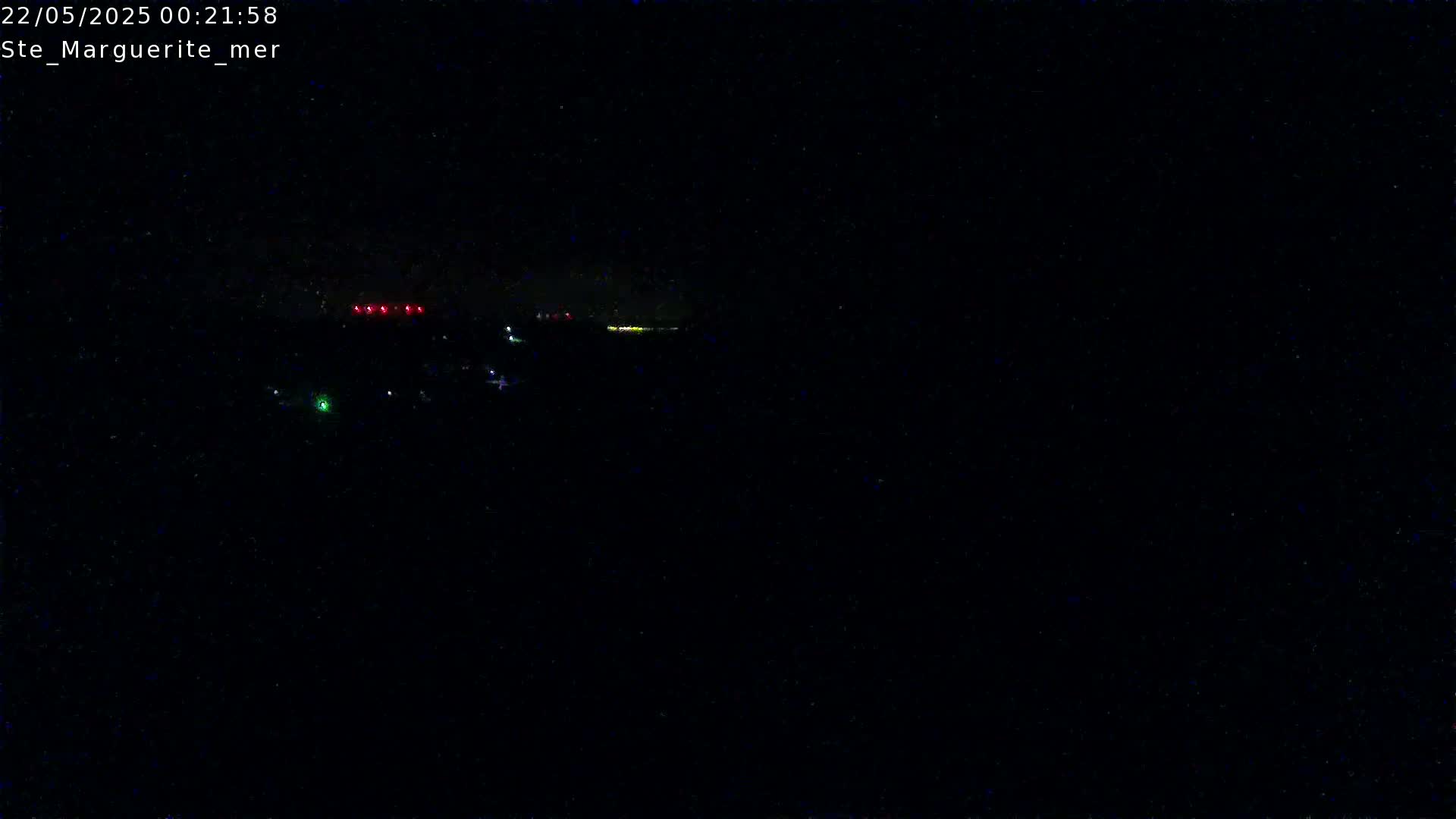 A nighttime view of a dark landscape with a few faint lights visible in the distance.