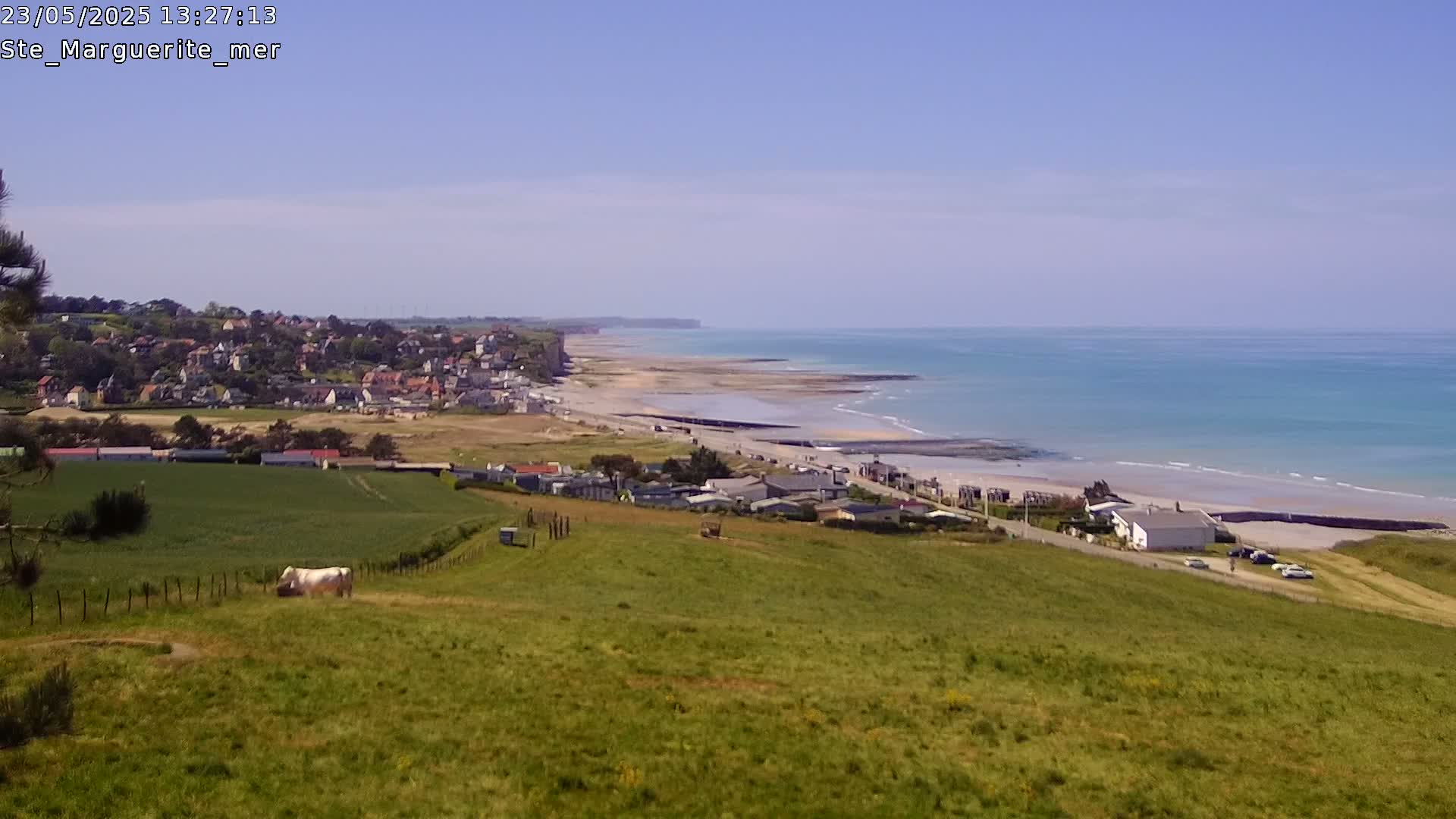 A coastal town sits nestled beside a long, sandy beach and a calm, blue ocean under a clear sky.
