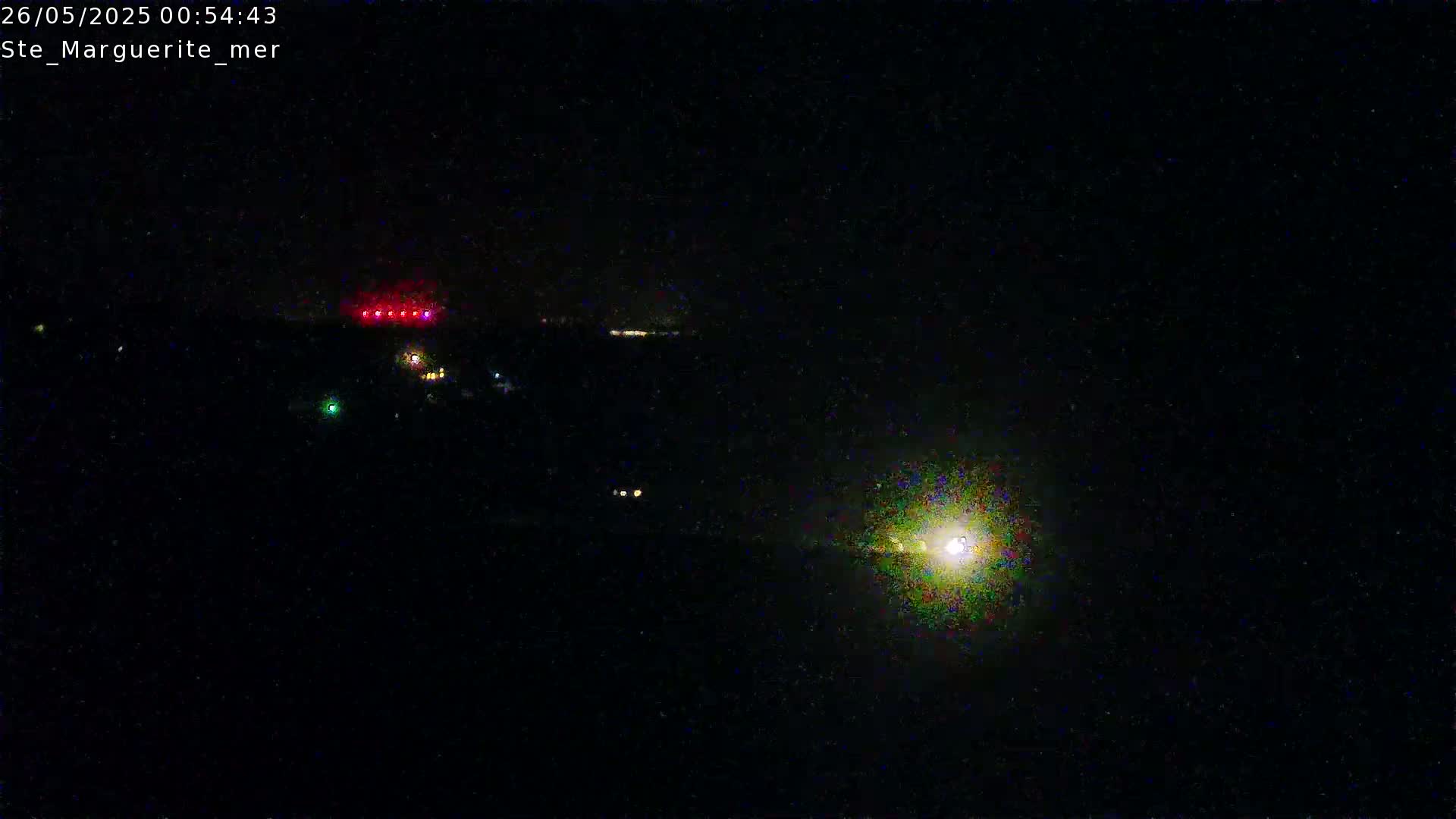 A nighttime, dark scene shows distant lights in the background and a bright light source in the foreground under a clear, dark sky.
