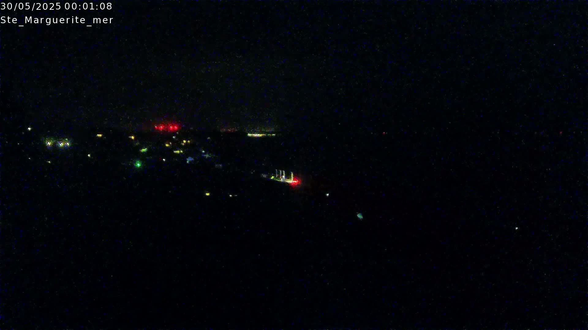 A nighttime long shot shows a dark landscape with scattered lights and a faint red light possibly from a vessel on the water.