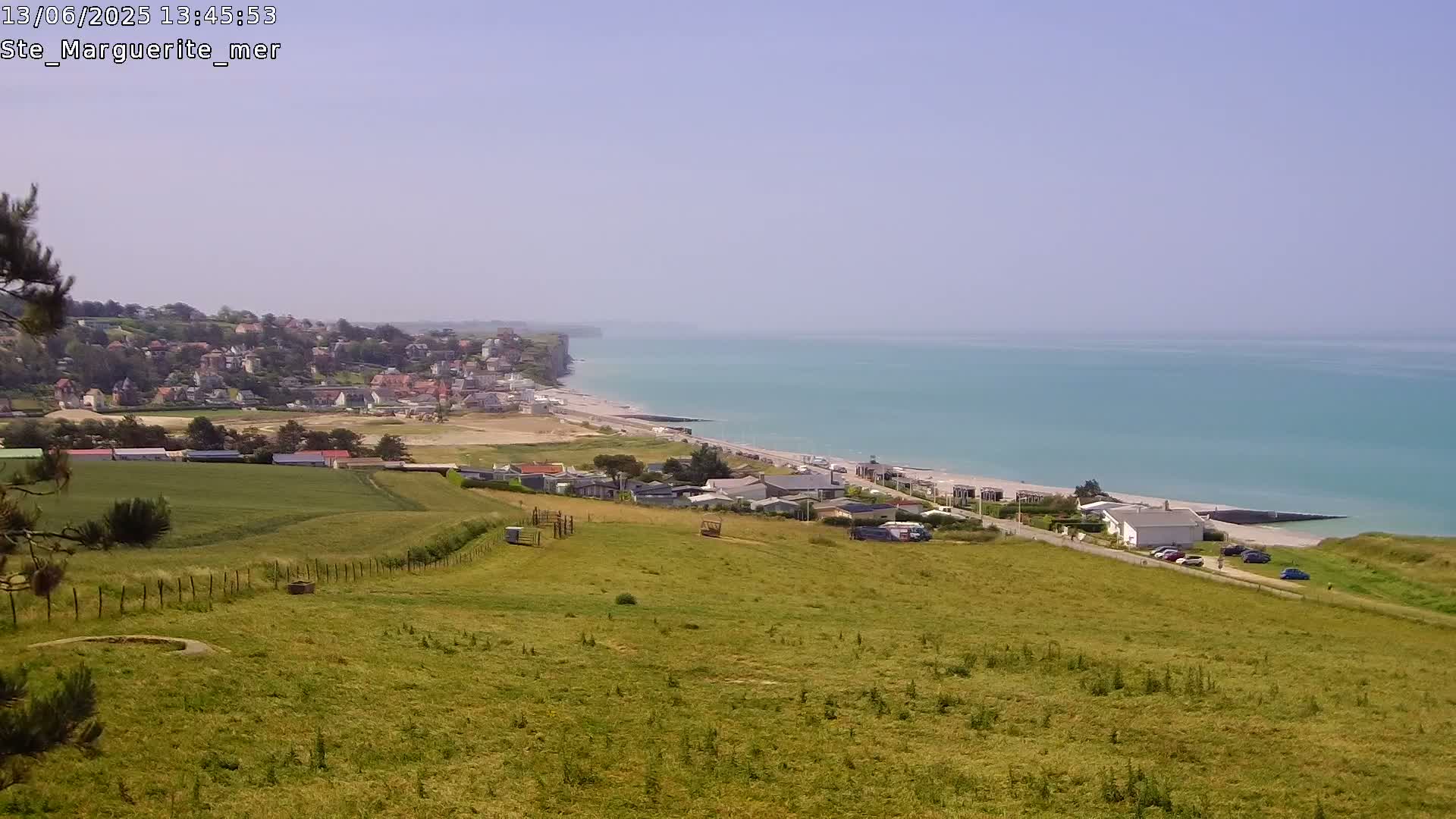 A coastal town nestled against high cliffs overlooks a calm, turquoise sea under a clear sky.