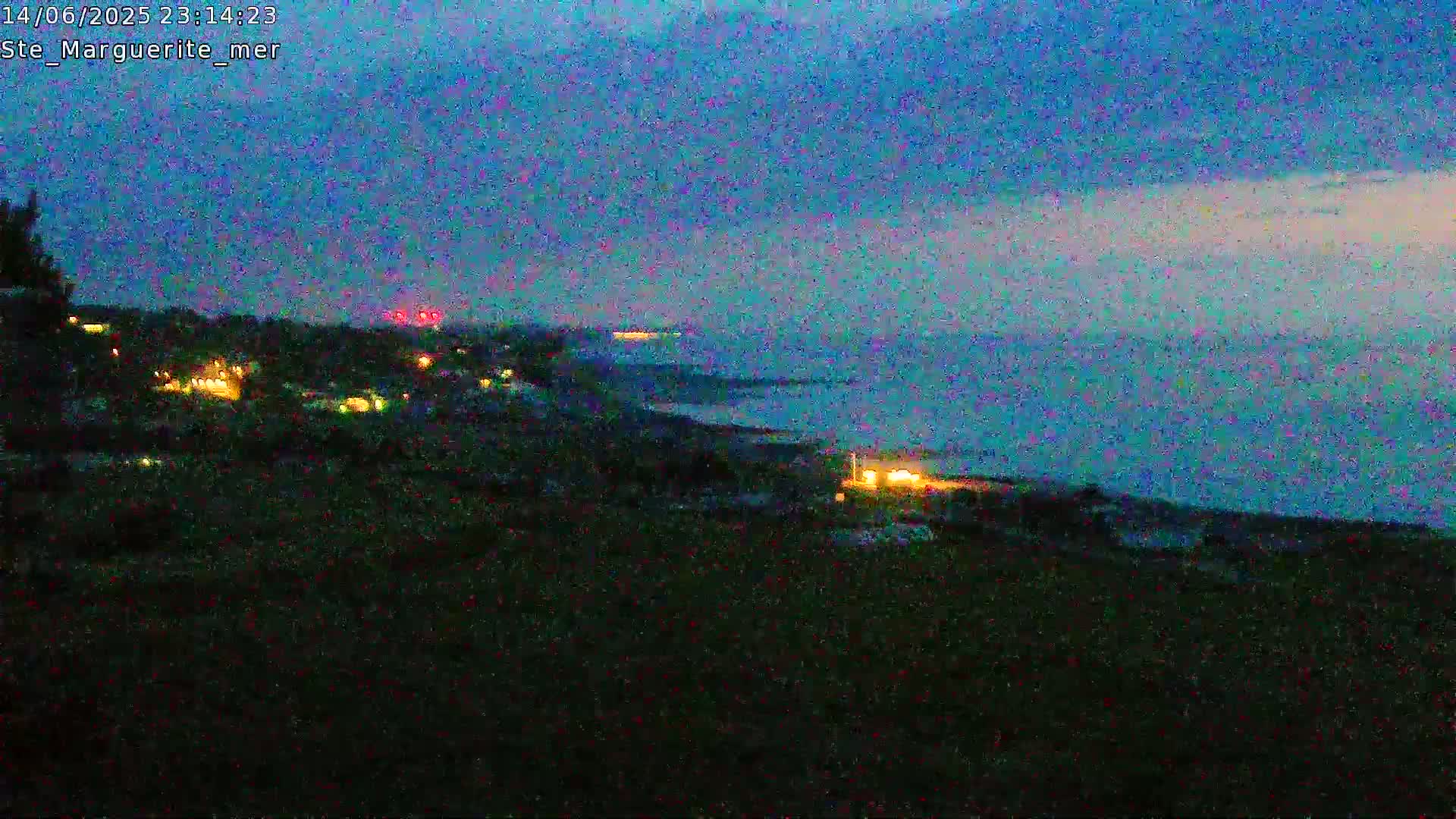 A pastoral scene of sheep grazing in a field overlooking a coastline with a town and cliffs under an overcast sky.