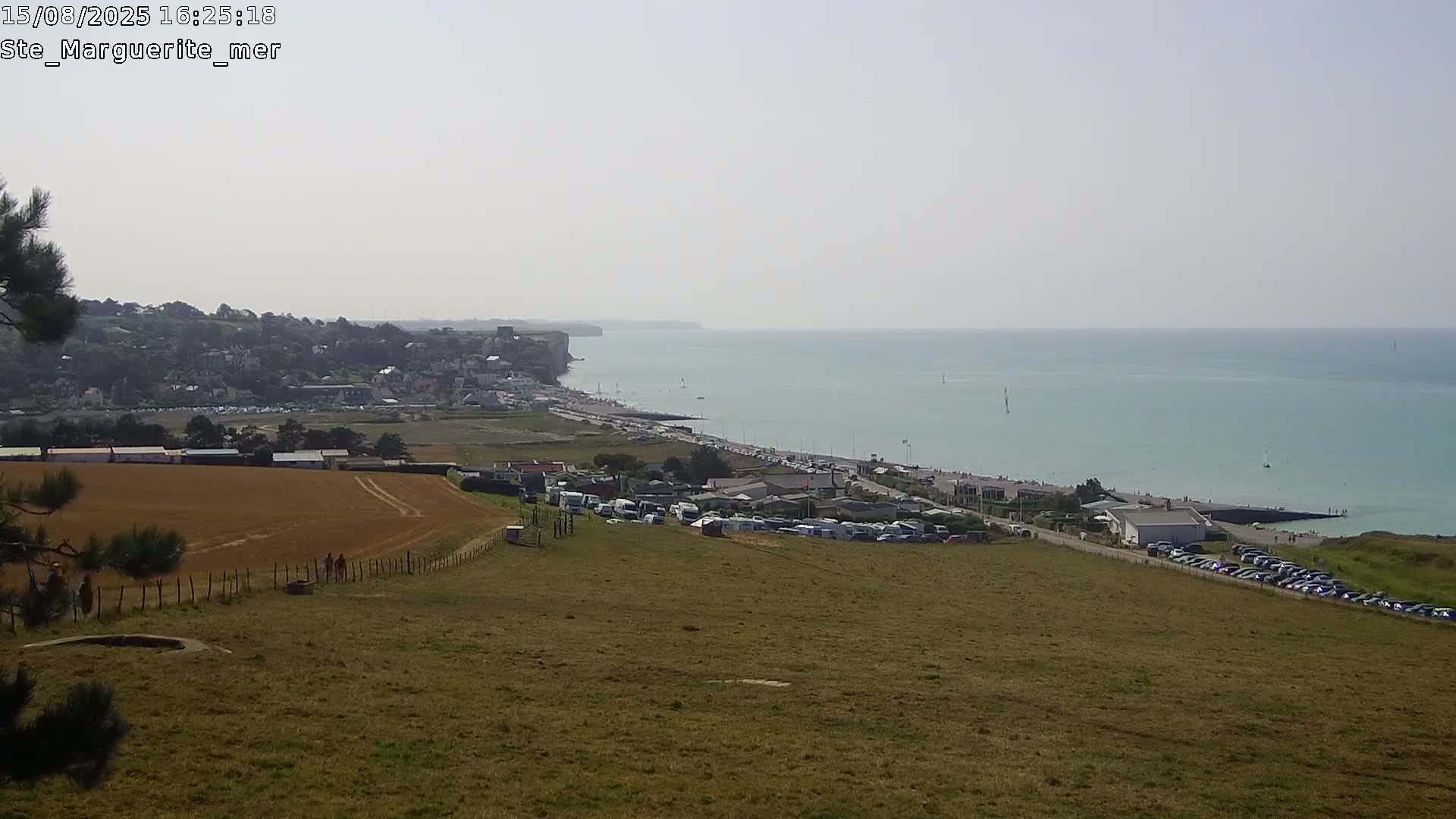 A coastal town is visible from a high vantage point on an overcast day, overlooking a wide expanse of sandy beach and calm sea.