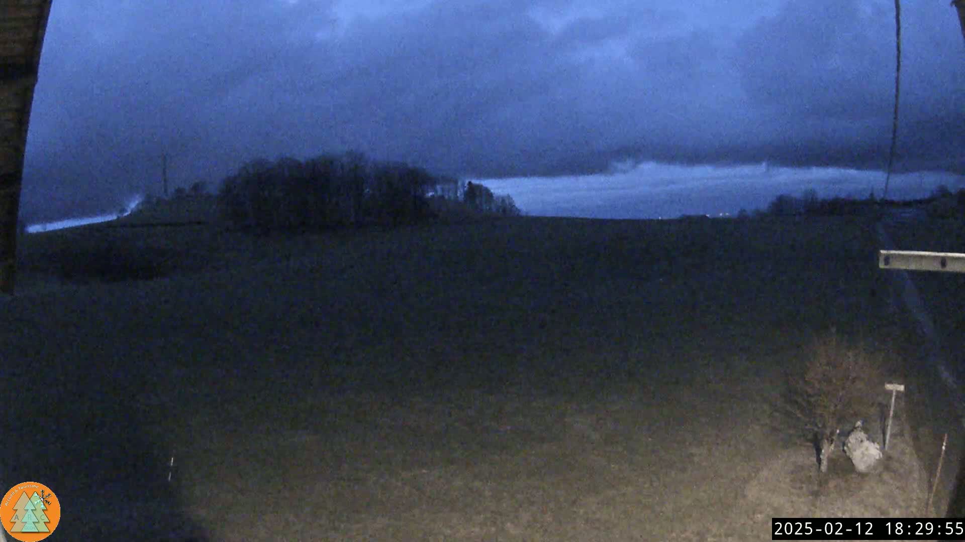 A dark, flat field stretches out under a mostly cloudy, twilight sky, with a line of trees visible in the distance.