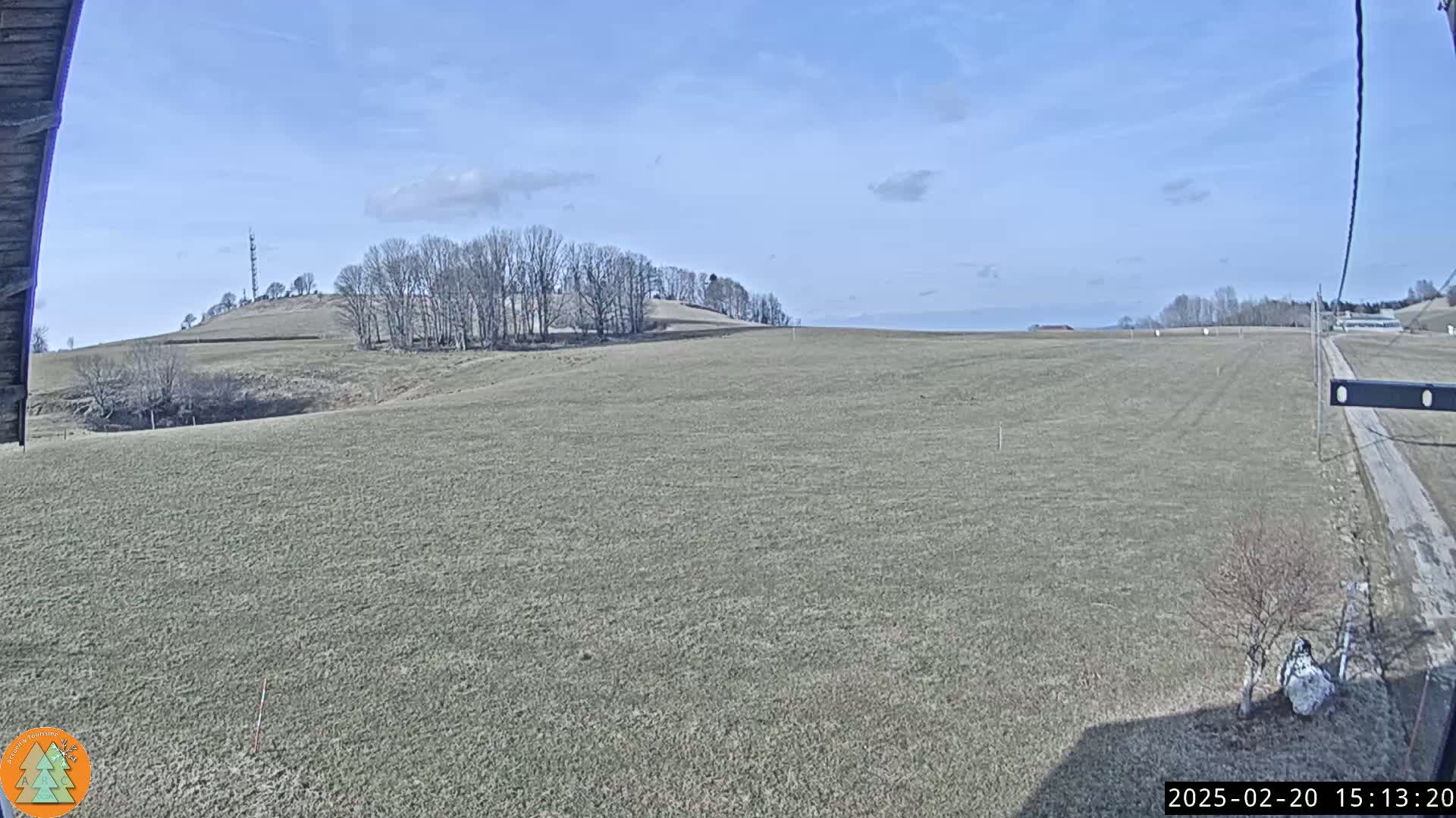 A large, flat field stretches to a distant hill under a mostly clear, sunny sky.