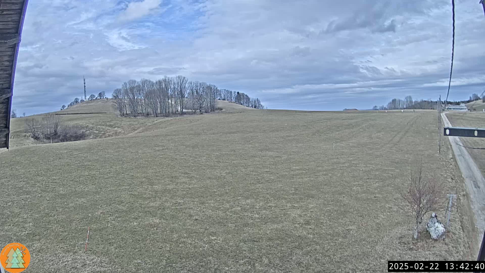 A flat, brown field stretches to a gently rolling hill under a mostly cloudy sky.
