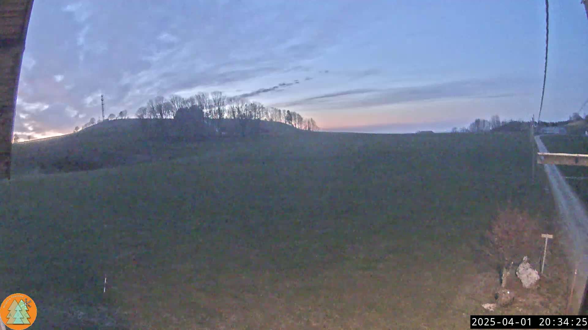 A flat, dark green field stretches out under a twilight sky, with a distant hill silhouetted against the fading light.