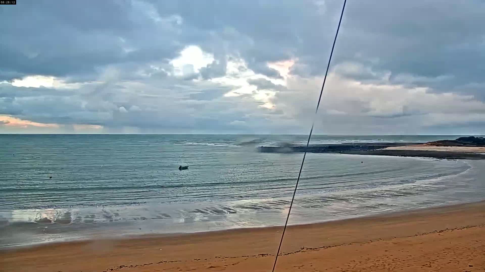 A sandy beach curves gently into a calm sea under a mostly cloudy sky.
