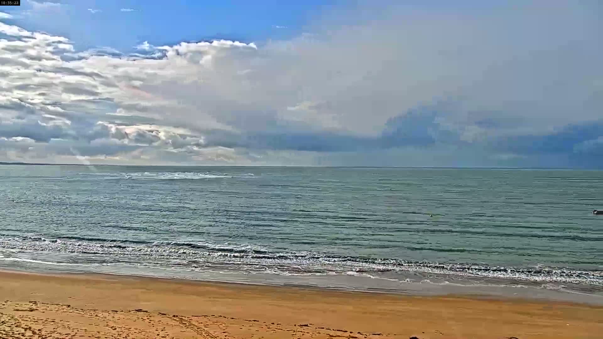A sandy beach meets a calm, gray-green ocean under a partly cloudy sky.