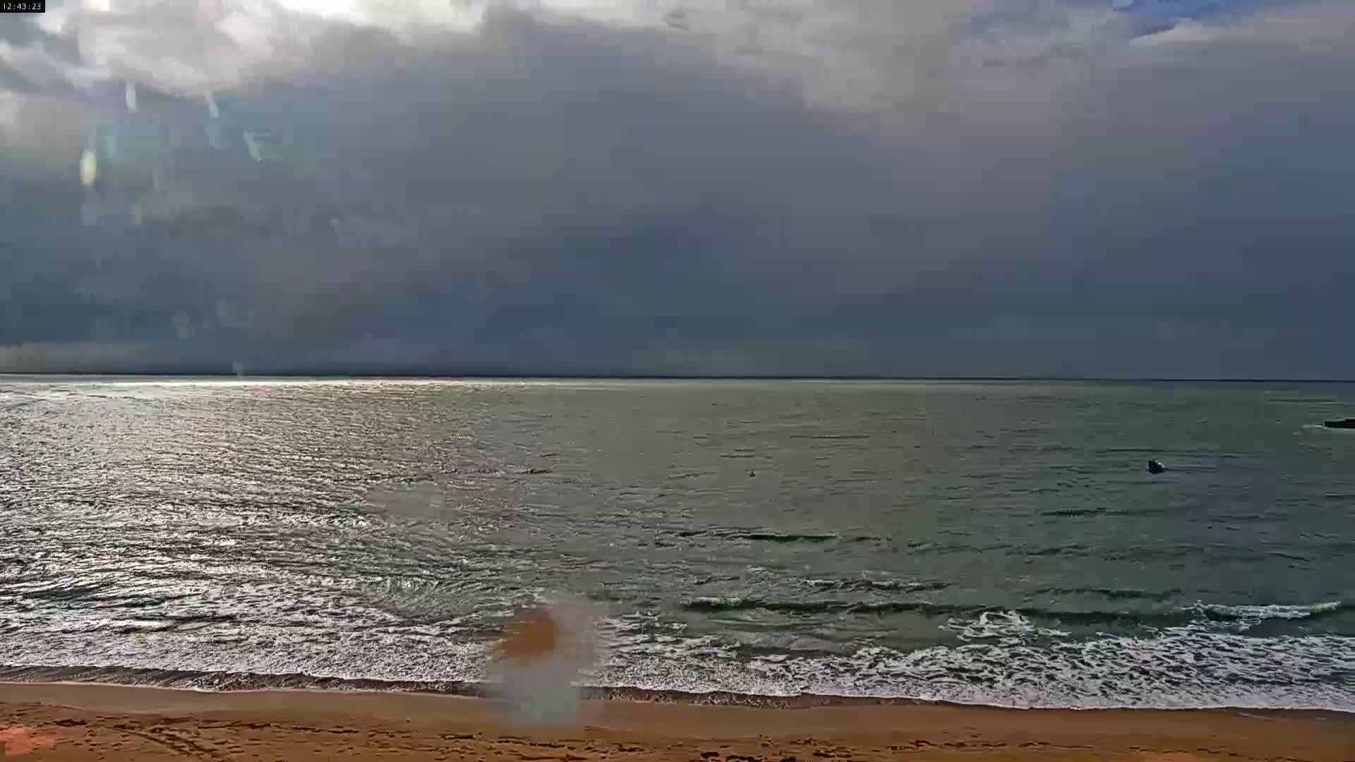 A sandy beach meets a somewhat choppy sea under a mostly cloudy sky.