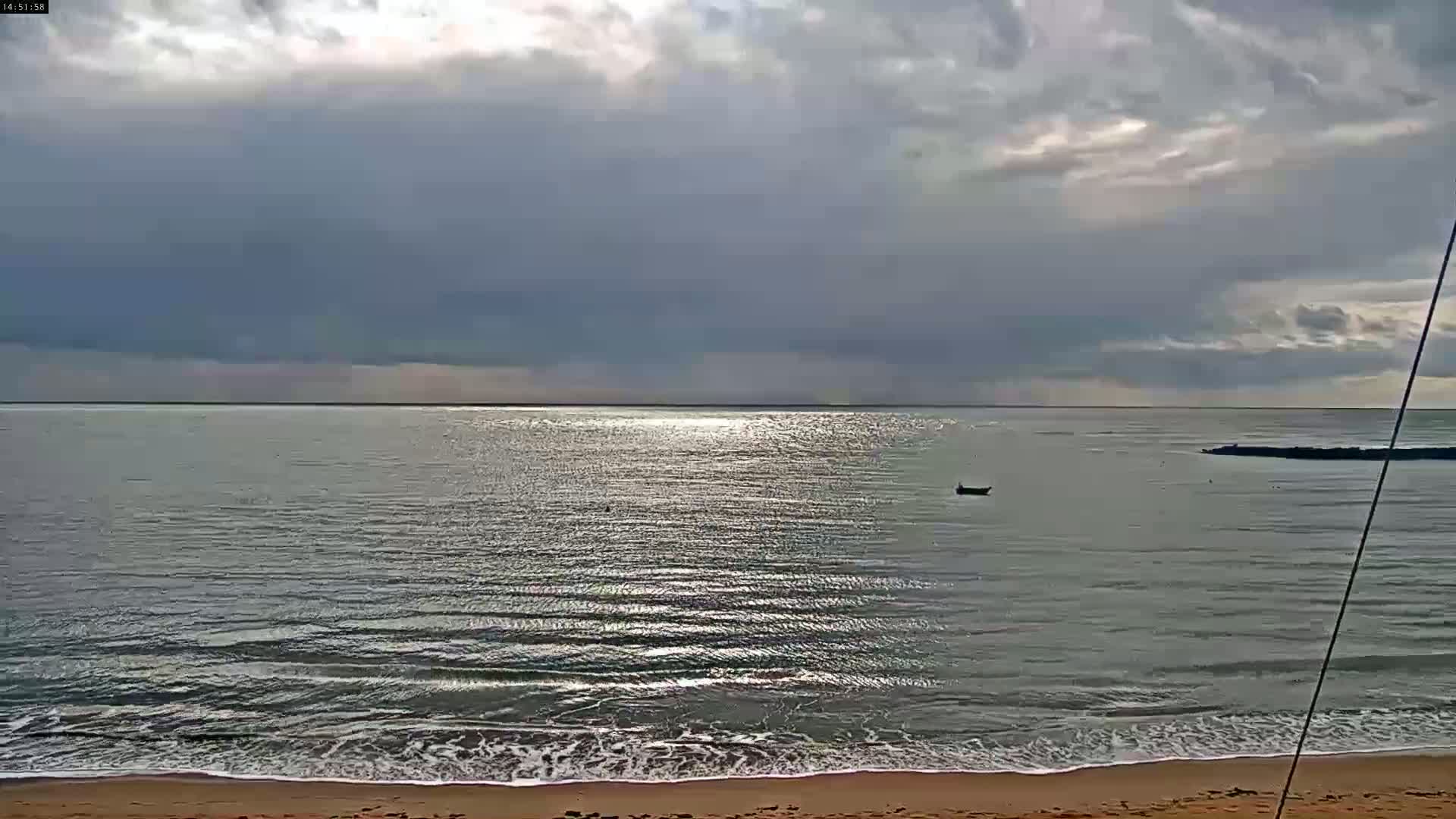 A calm sea with small waves laps a sandy beach under a mostly cloudy sky.