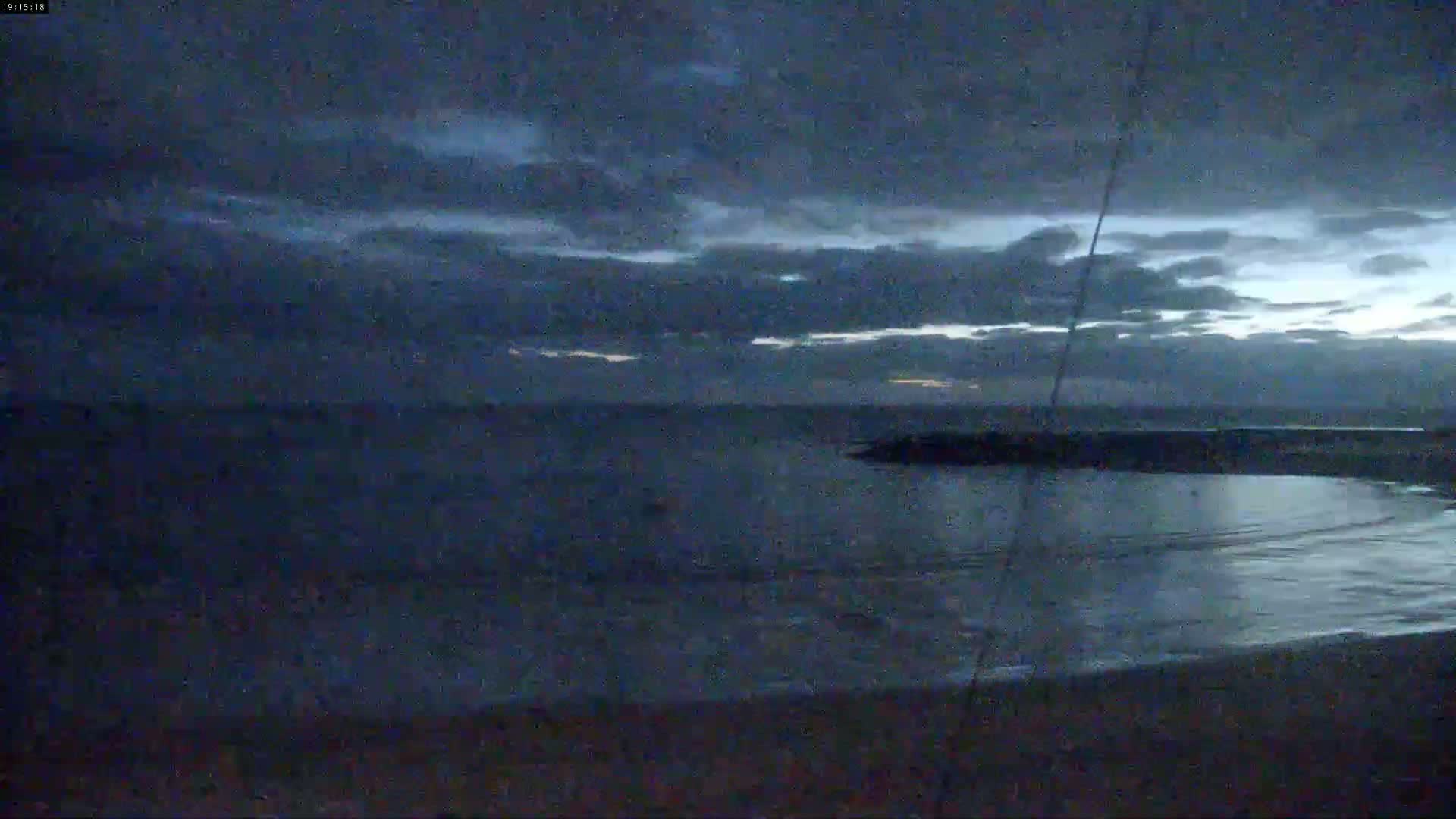 A dark, mostly cloudy twilight sky over a calm body of water with a dark landmass visible in the middle distance.