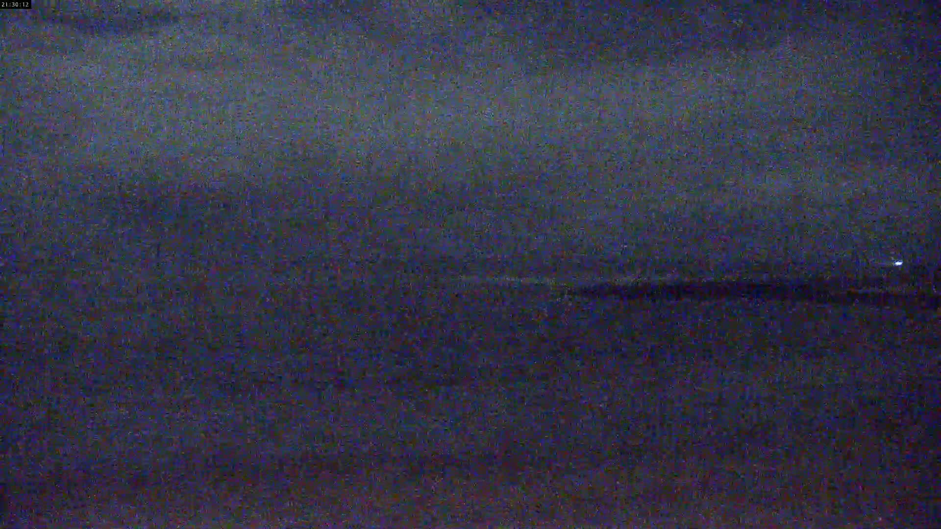 A dark, blurry nighttime image shows a mostly flat, dark horizon line, possibly over water under an overcast sky.