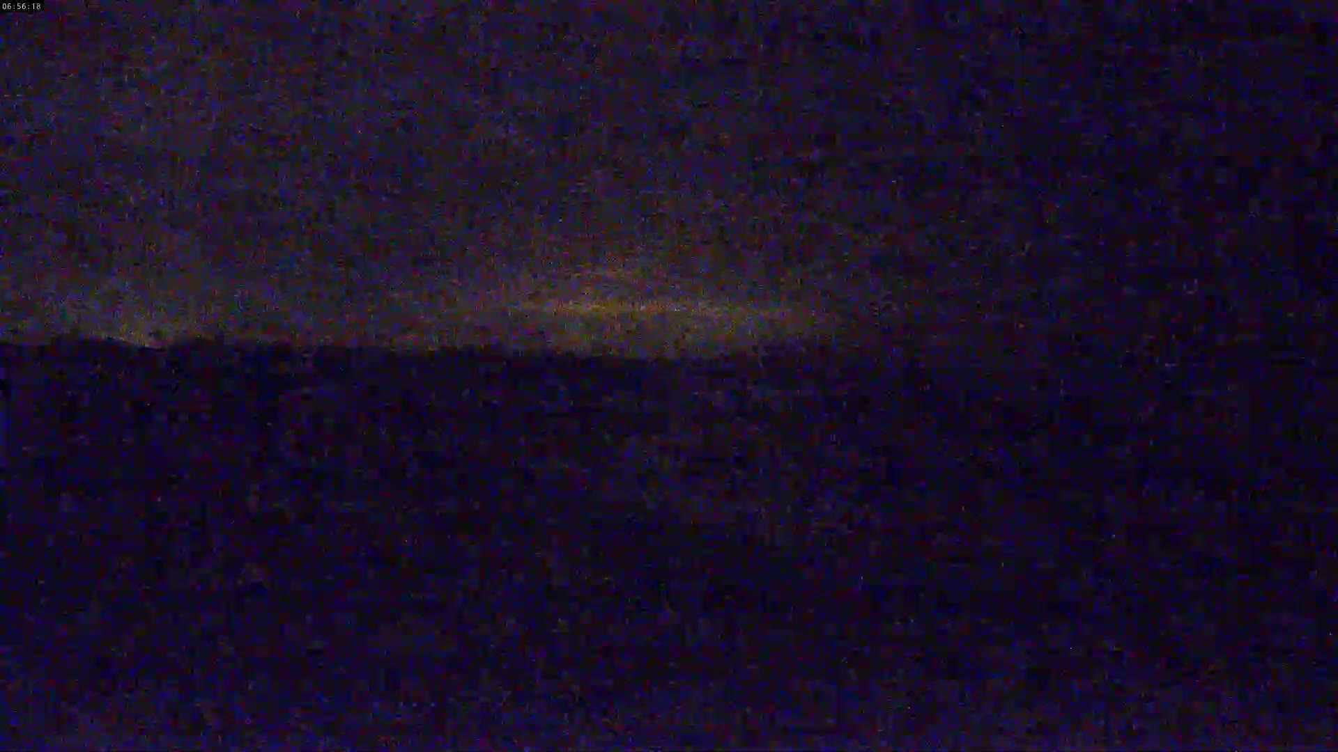 A dark, nighttime landscape shows a faintly lit horizon under a mostly cloudy sky.