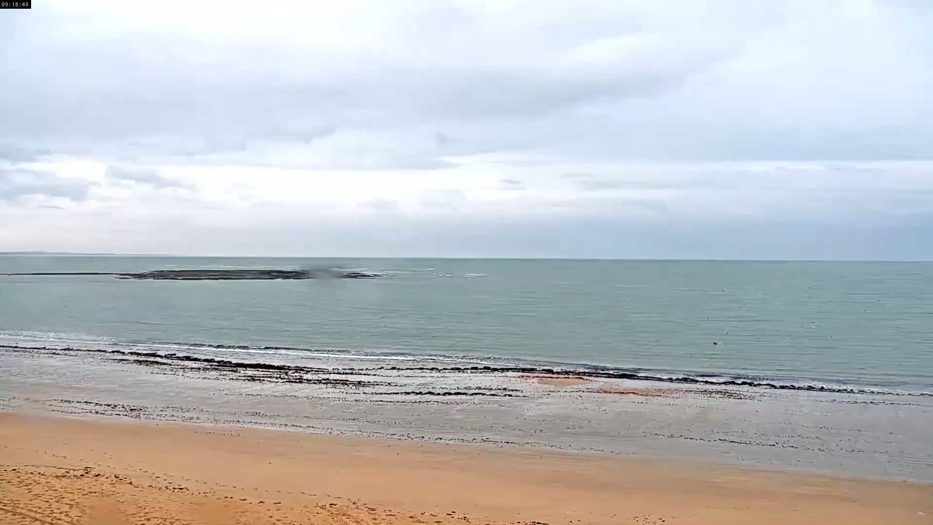 A sandy beach slopes down to a calm, grey-green sea under a cloudy sky.