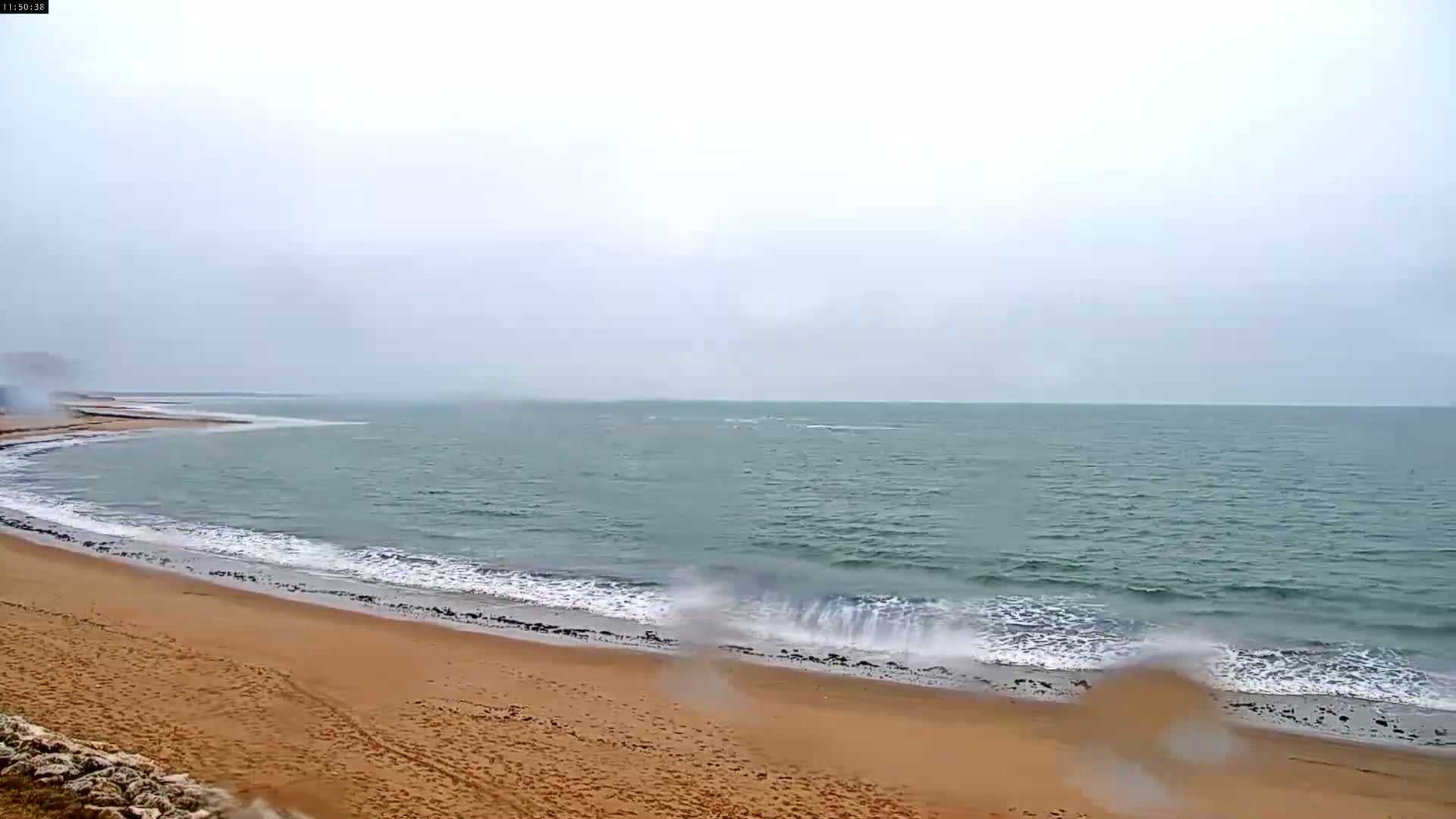 A sandy beach with small waves rolls onto the shore on an overcast day.