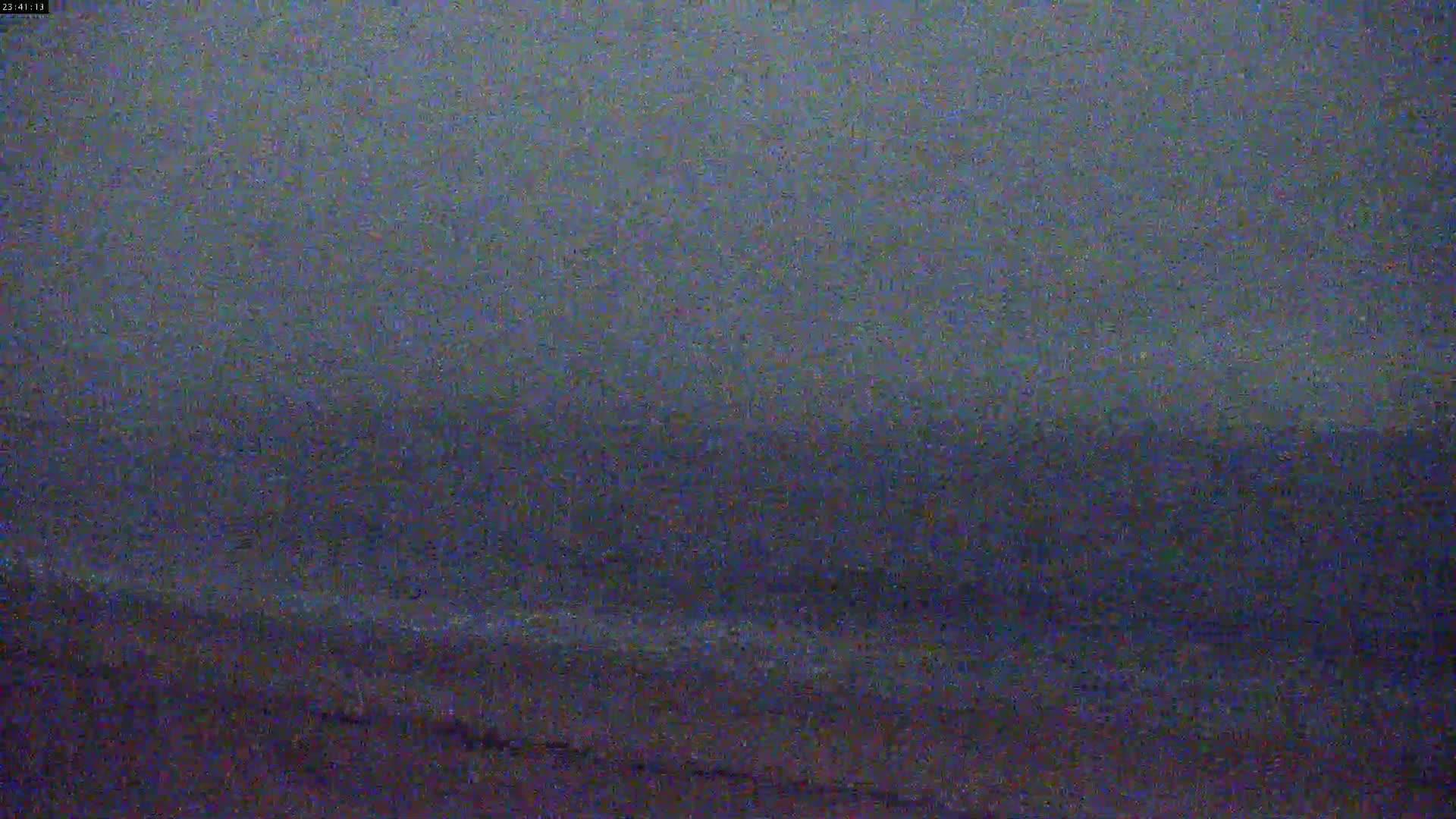 A blurry, dark image shows a possibly nighttime view of a beach and ocean under an overcast sky.