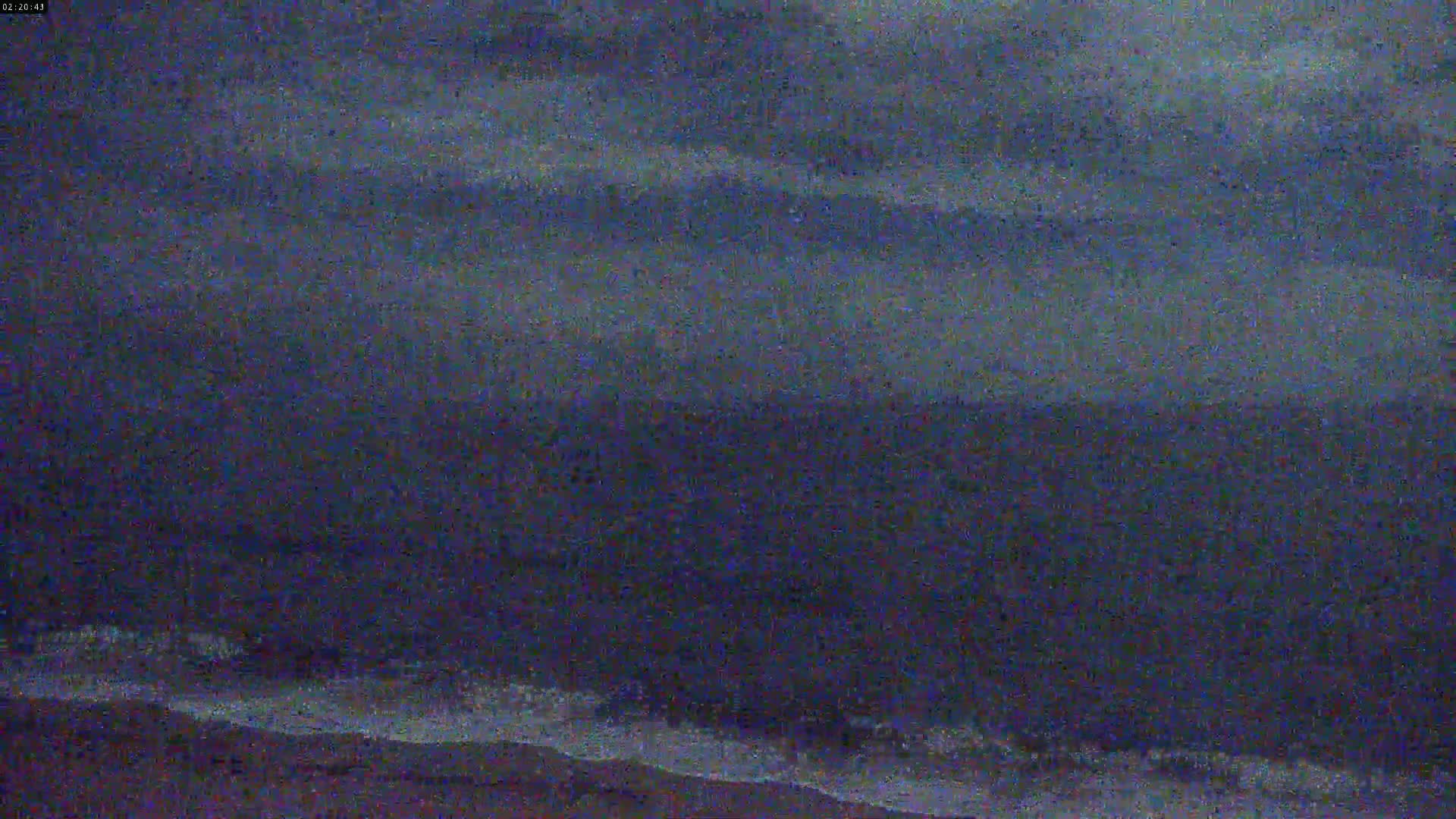 A dark, overcast sky hangs over a body of water with gently rolling waves at the shore.