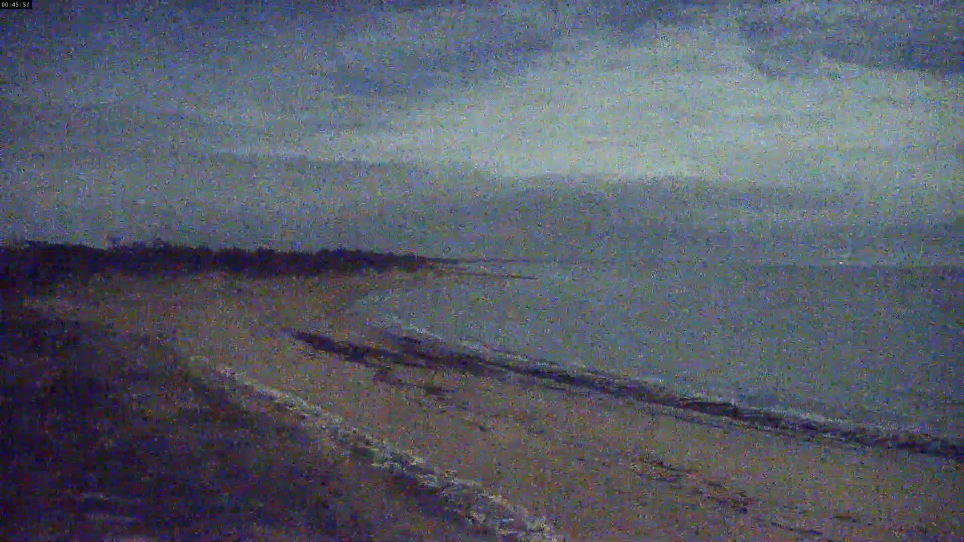 A sandy beach meets a calm, dark-grey sea under an overcast sky.