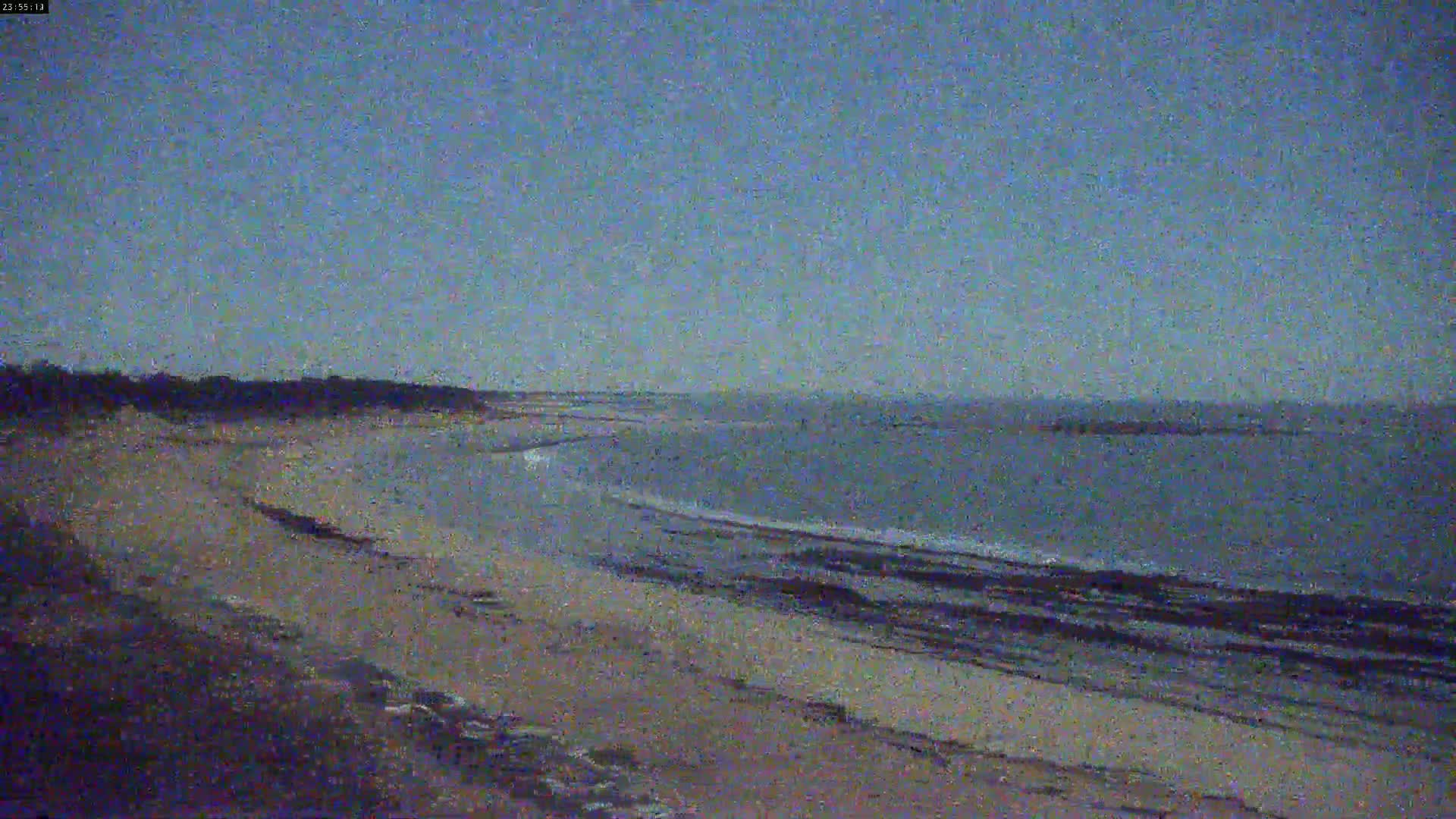 A sandy beach slopes down to a calm, gray ocean under a twilight sky.