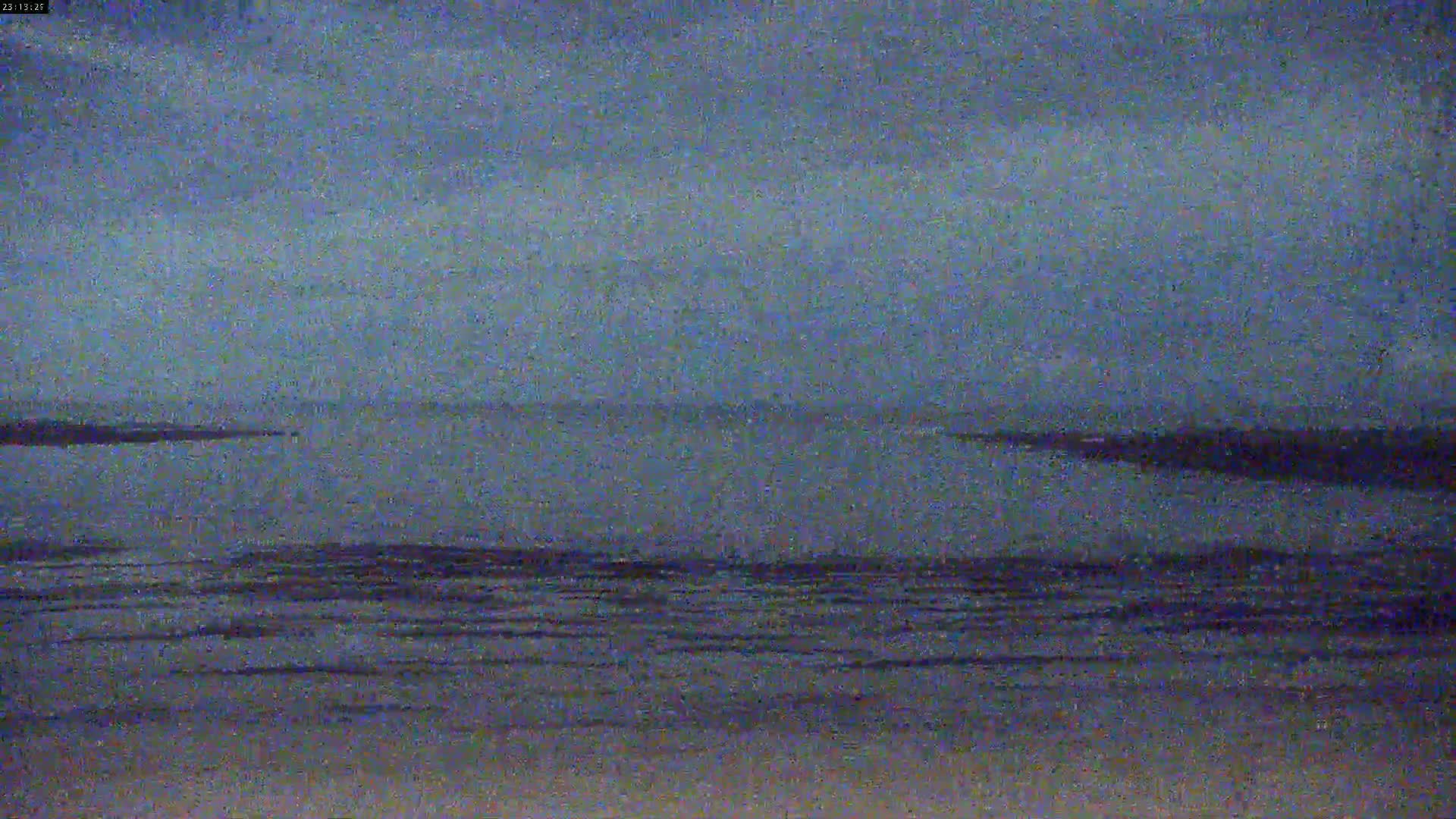 A dark, overcast sky hangs over a calm body of water with a dark shoreline.