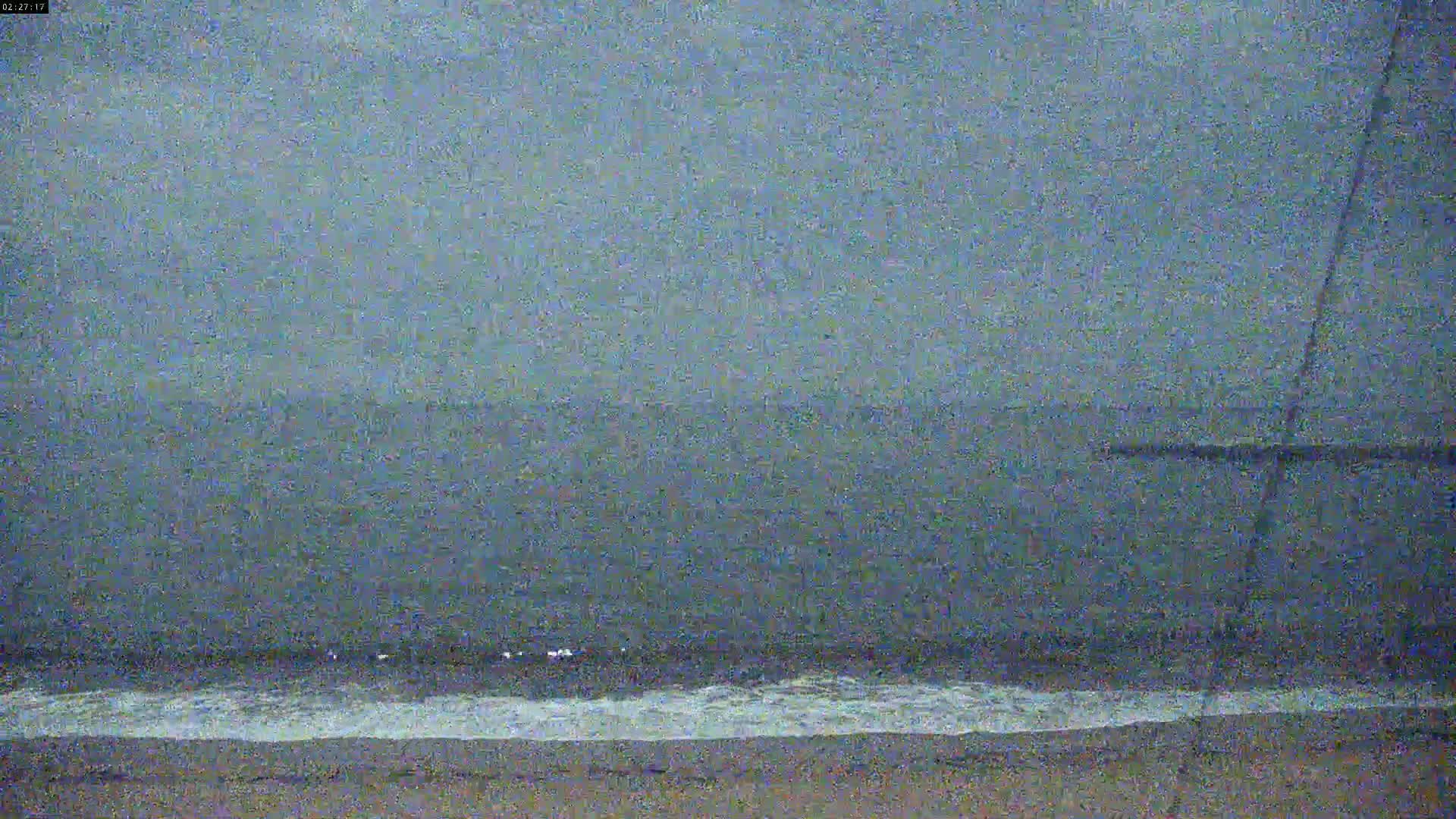 A dark, overcast sky looms over a calm ocean meeting a sandy beach.