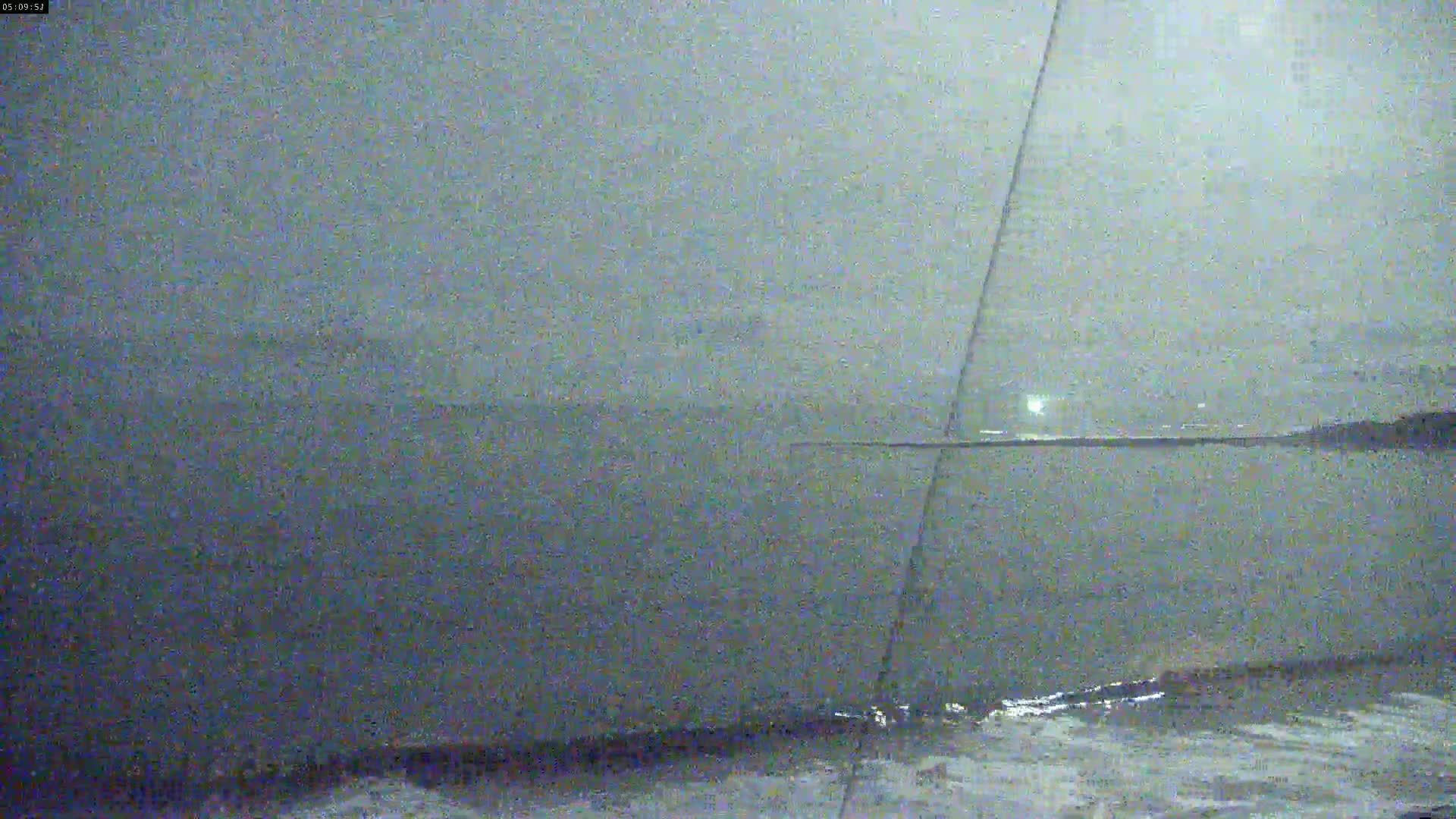 A dark, overcast sky looms over a calm body of water with a distant shoreline visible under low-light conditions.