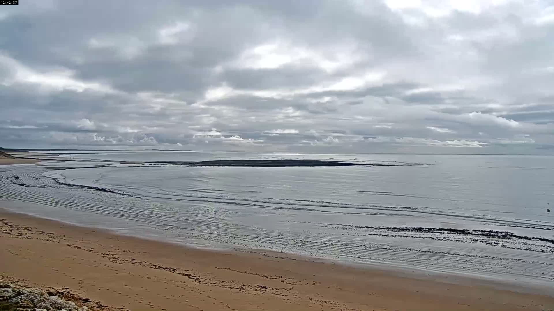 A sandy beach stretches out to a calm, grey sea under a mostly cloudy sky.