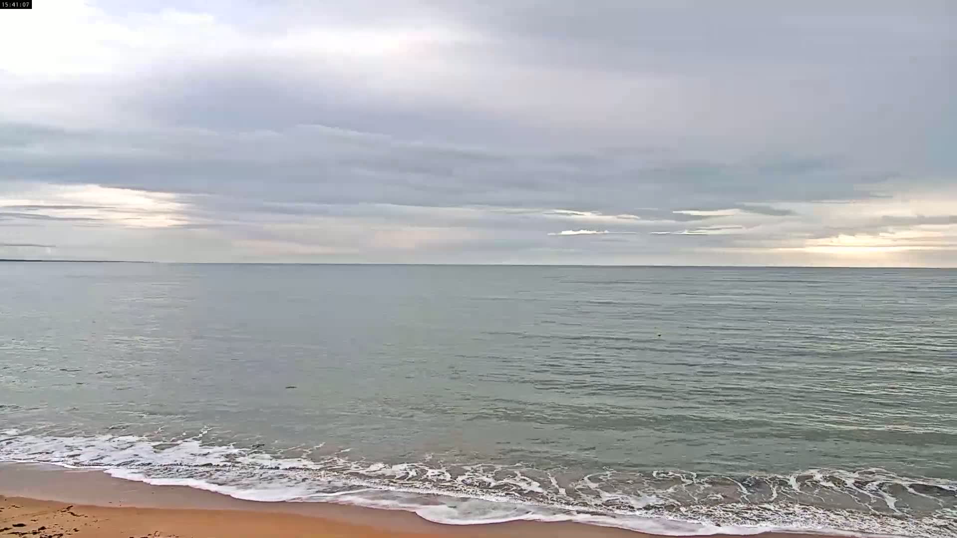 A sandy beach meets a calm, gray-green sea under a mostly cloudy sky.