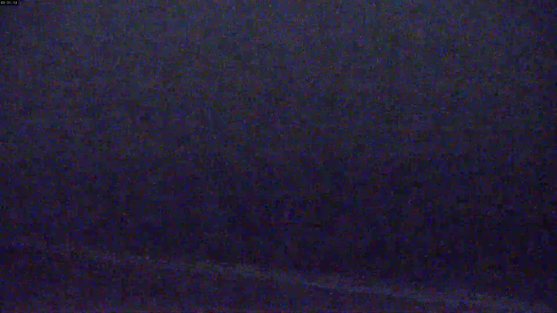 The image shows a dark, blurry view of a nighttime scene, possibly outdoors with light rain or snow.
