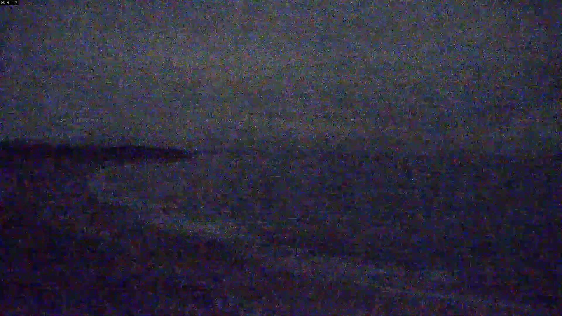 A dark, possibly nighttime, image shows a blurry view of a body of water with a dark shoreline in the distance under a dark, overcast sky.