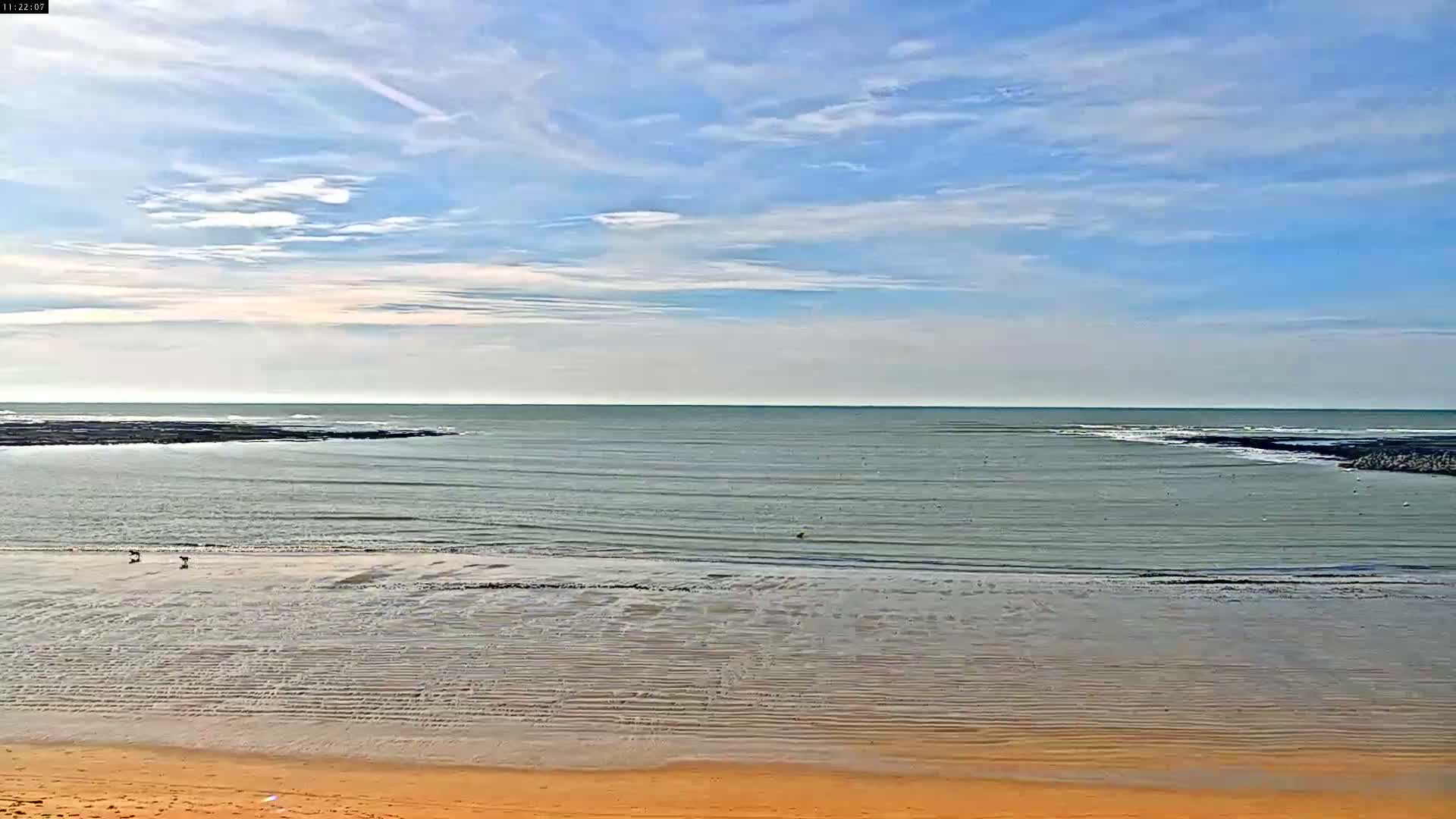 A calm sea with a mostly clear sky and a sandy beach stretches out to a distant horizon.