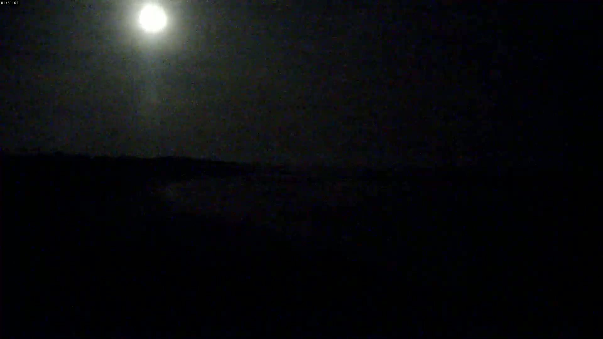 A bright moon illuminates a dark, mostly featureless landscape under a night sky.