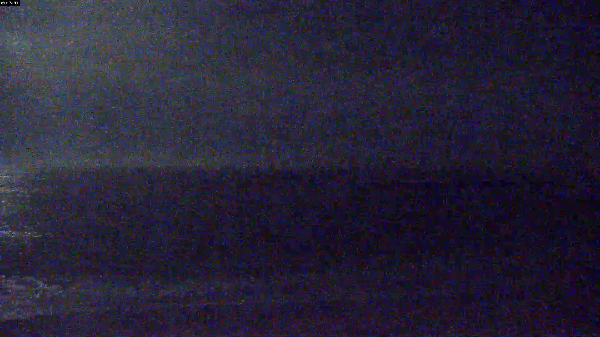 A dark, blurry image shows an indistinct dark landscape under a mostly clear, dark night sky.