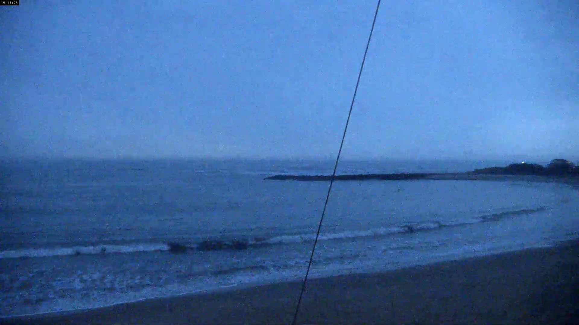 A dark, overcast sky hangs over a calm ocean with small waves lapping a sandy shore.