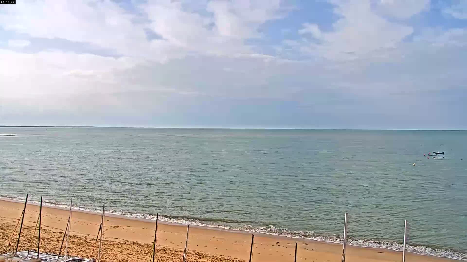 A sandy beach meets a calm, light-green sea under a mostly cloudy sky.