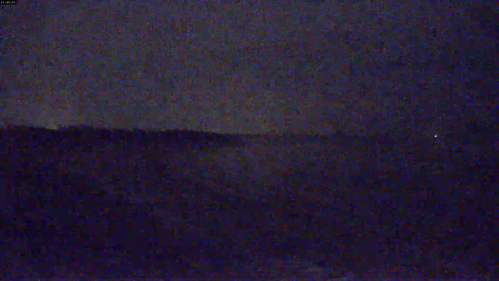A dark, nighttime scene shows a body of water and a distant shoreline under a mostly clear sky.
