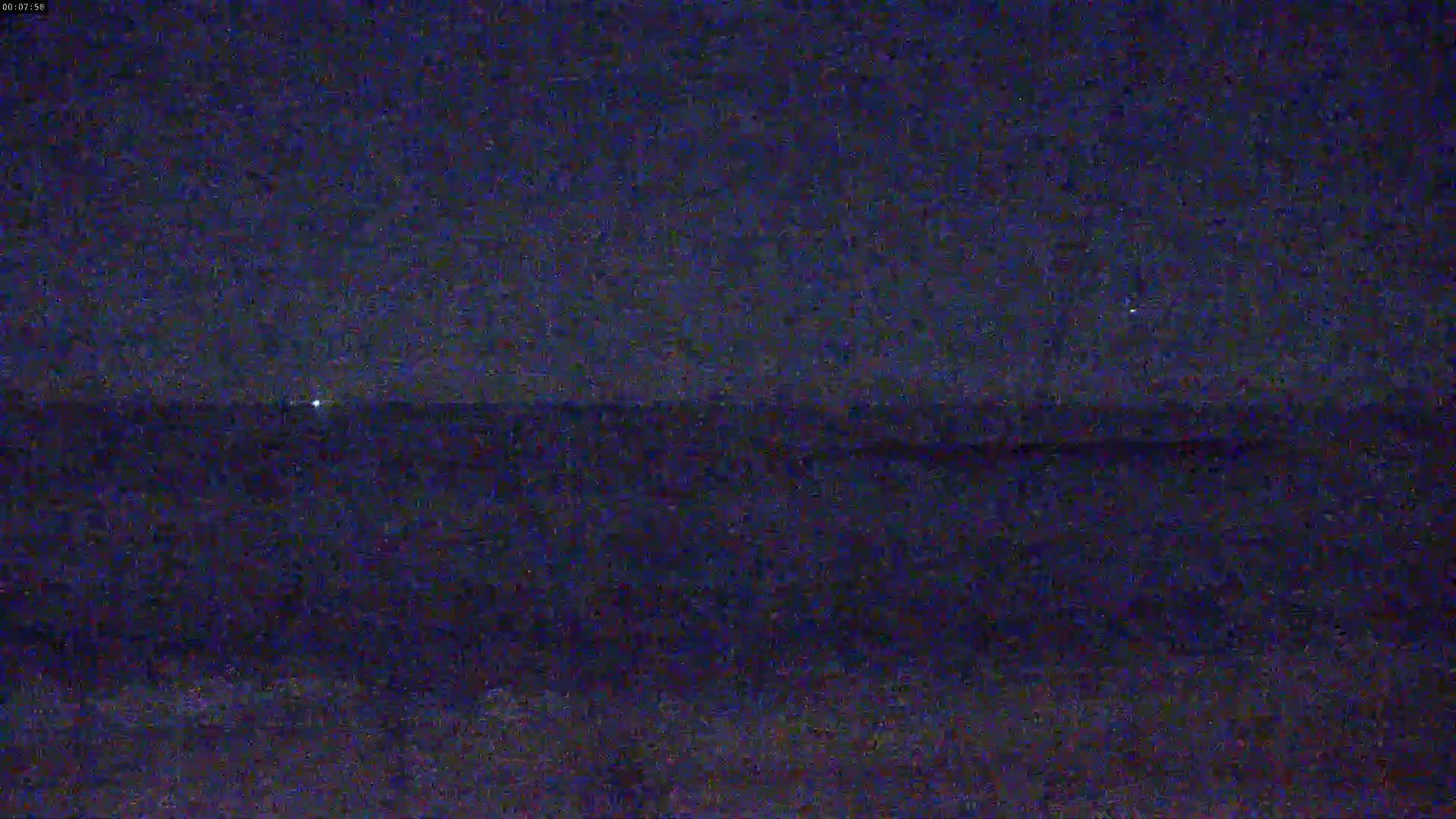 A dark, nighttime view shows a distant horizon line, possibly of the ocean, under a mostly clear sky.