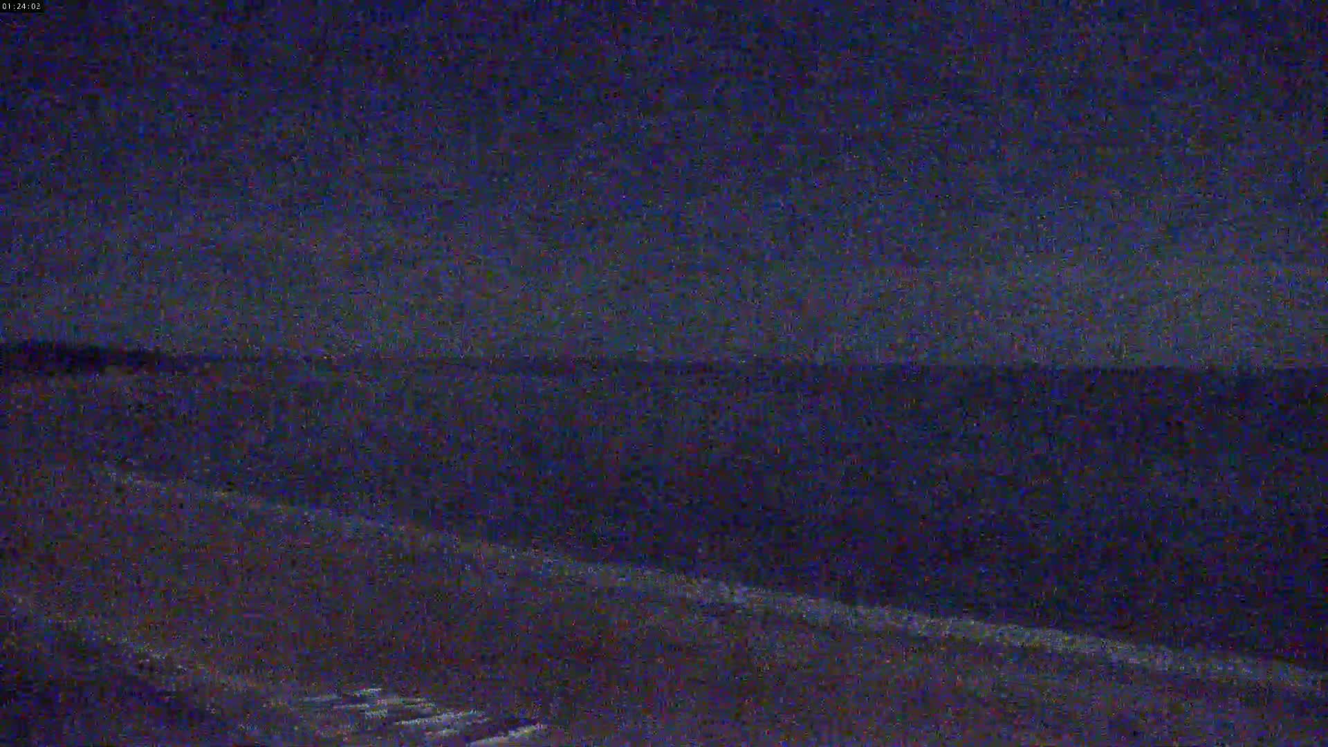 A dark, nighttime landscape shows a flat, dark expanse of land under a mostly clear, dark sky.