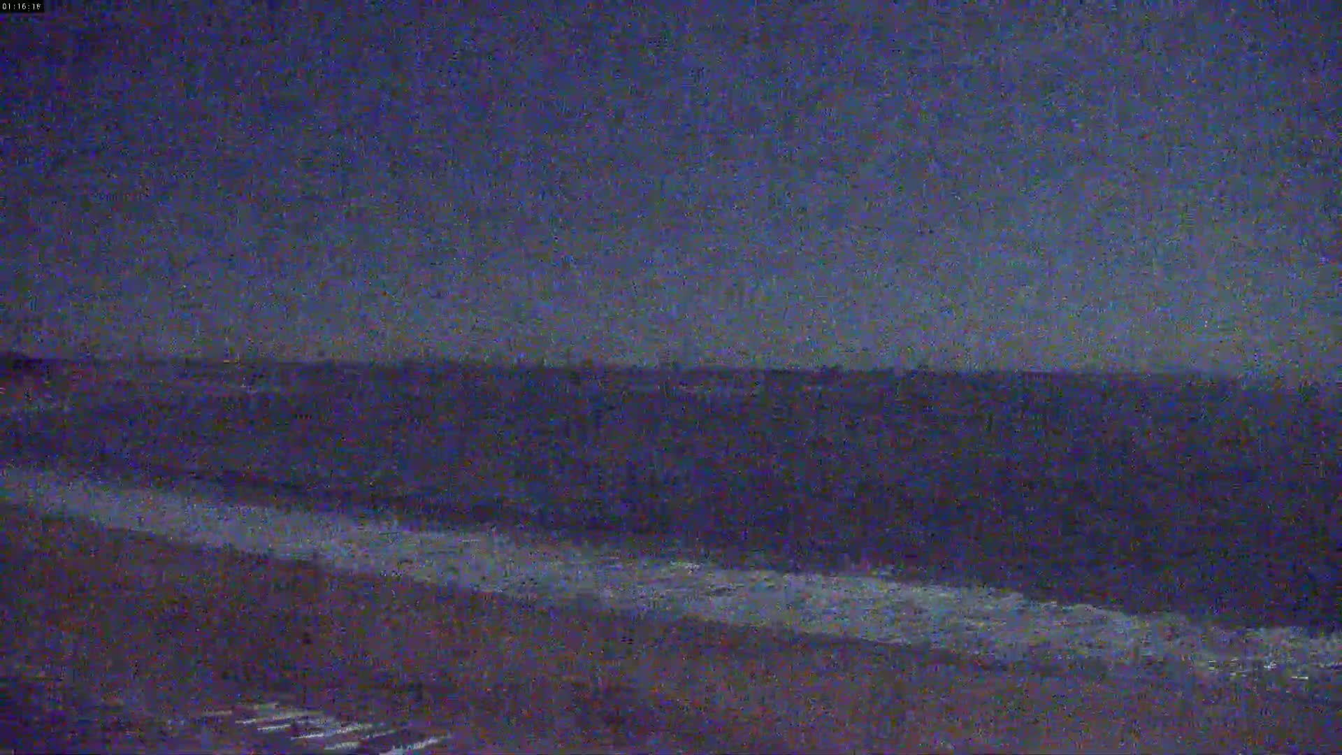 A dark beach at night shows gentle waves lapping the shore under a dusky sky.