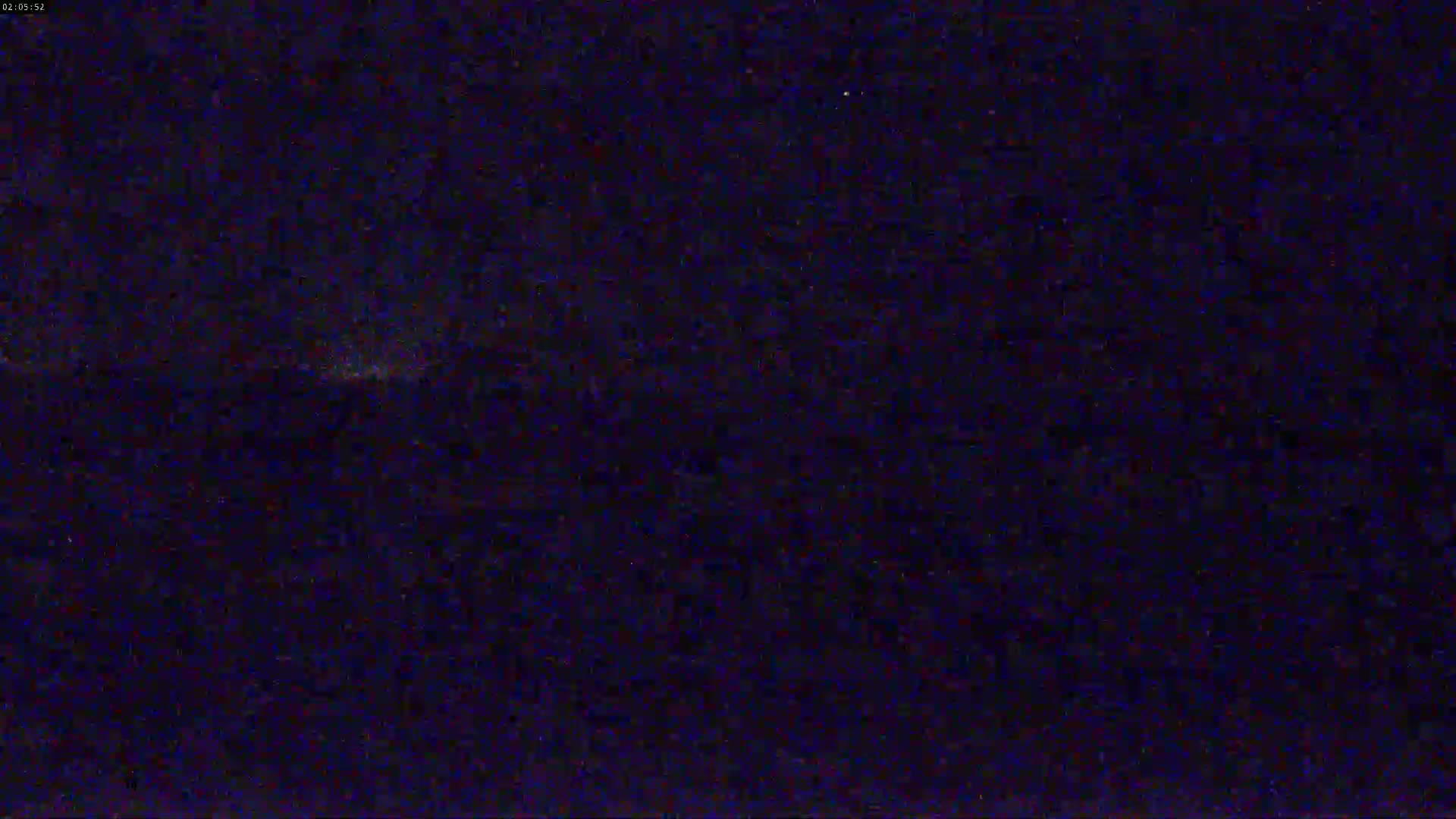 A dark, nighttime scene shows a faint, blurry light source on the horizon.