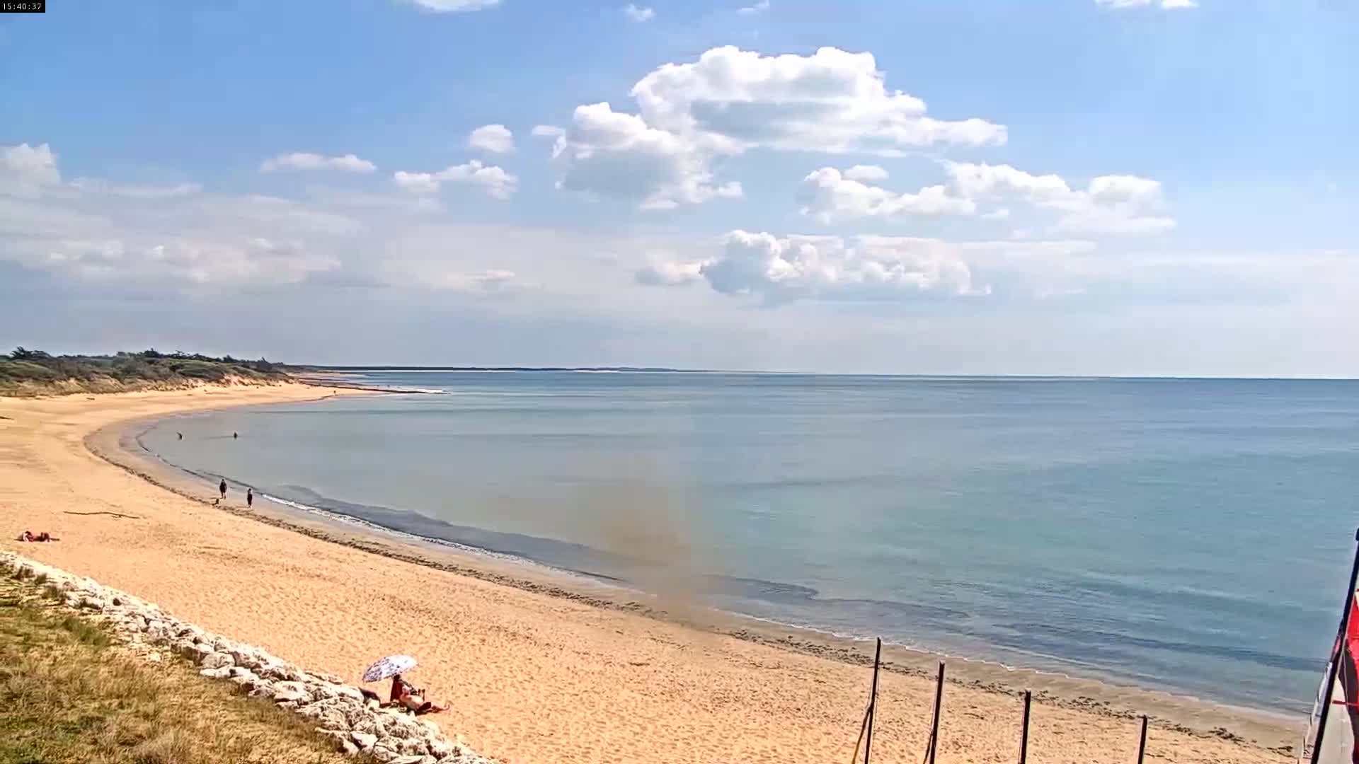 A sandy beach curves gently into a calm, light-blue ocean under a partly cloudy sky.